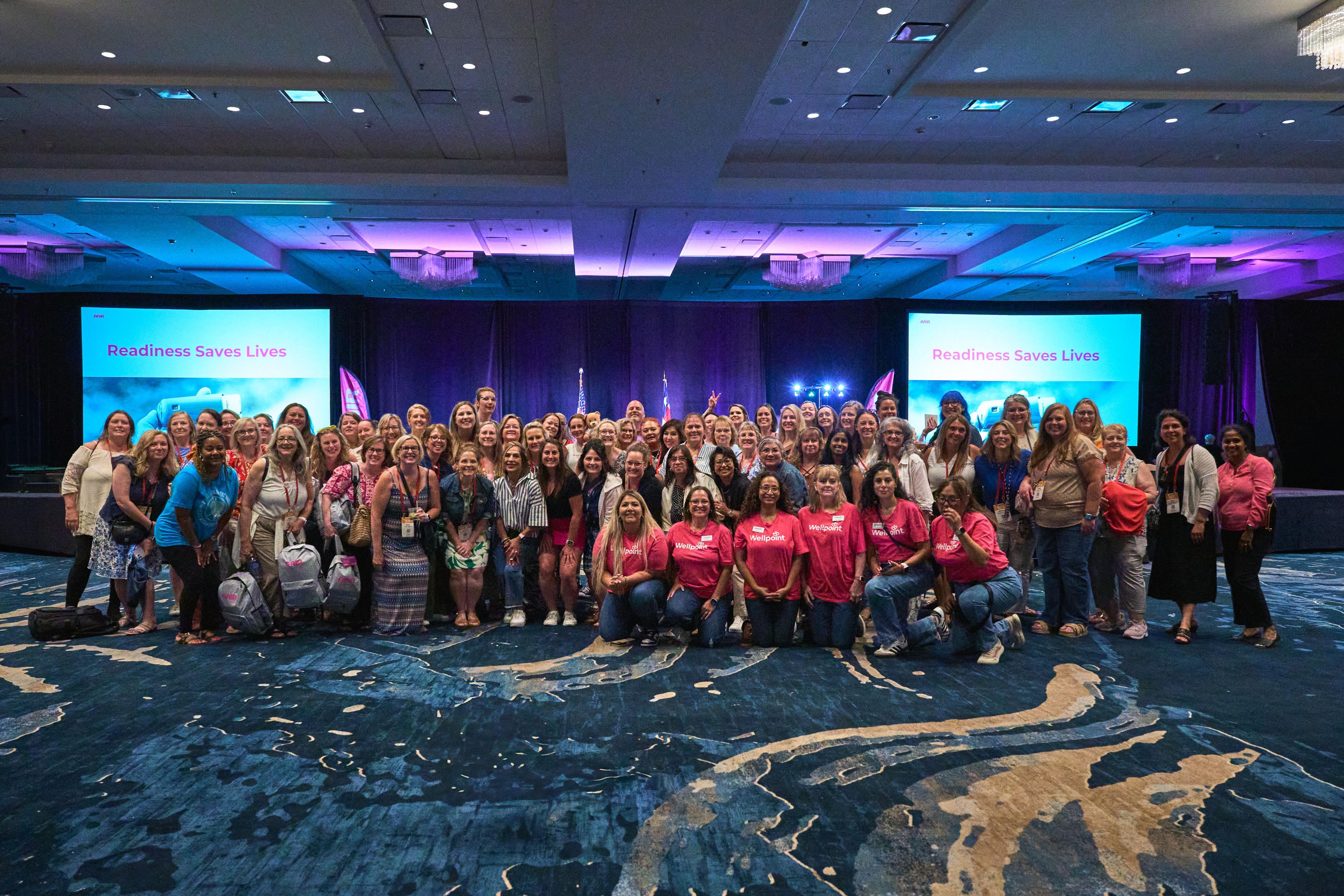 Large conference group photo, many in matching pink shirts, on a ballroom floor — Conventions & Tradeshows photography, Austin A large conference group photo, many in matching pink shirts, on a ballroom floor.