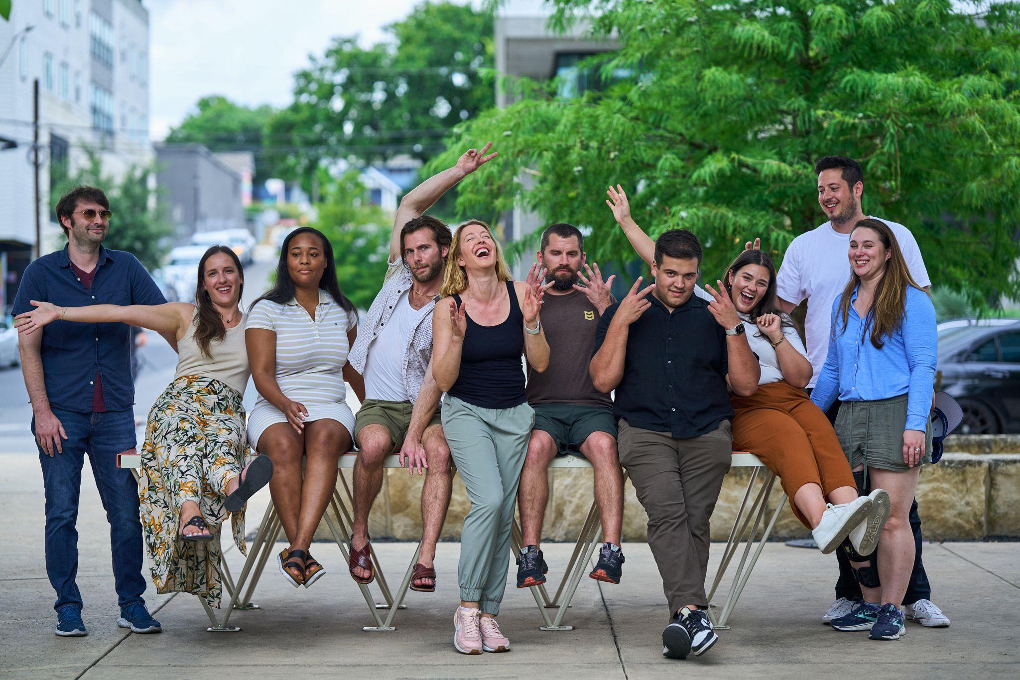 Group of colleagues sitting along an outdoor bench, laughing — Team offsite photography, Austin Group of colleagues sitting along an outdoor bench, laughing