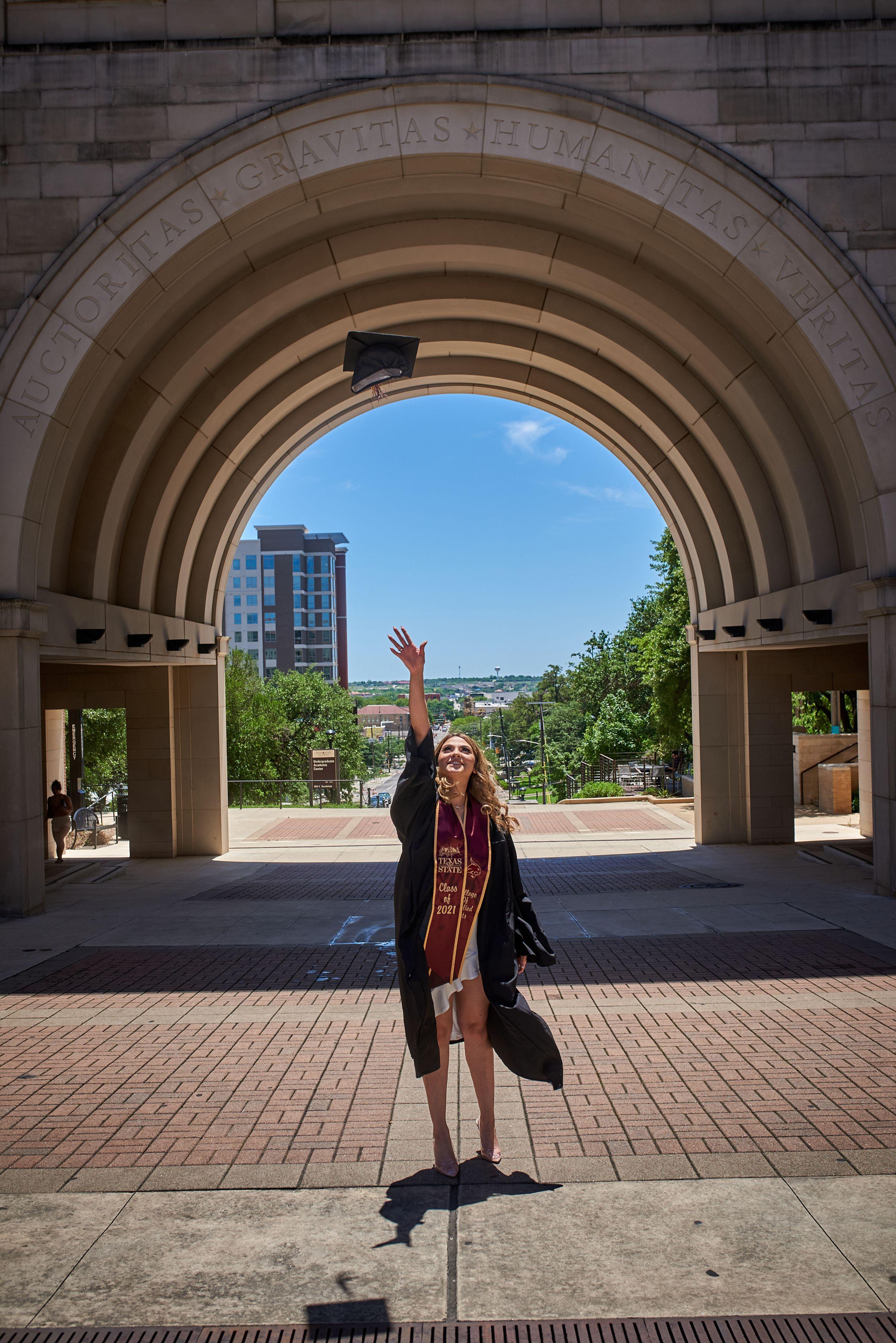 Graduate in cap and gown seated on a rail beside the campus steps at Texas State — Texas State University photography, Austin A graduate in cap and gown seated on a rail beside the campus steps at Texas State