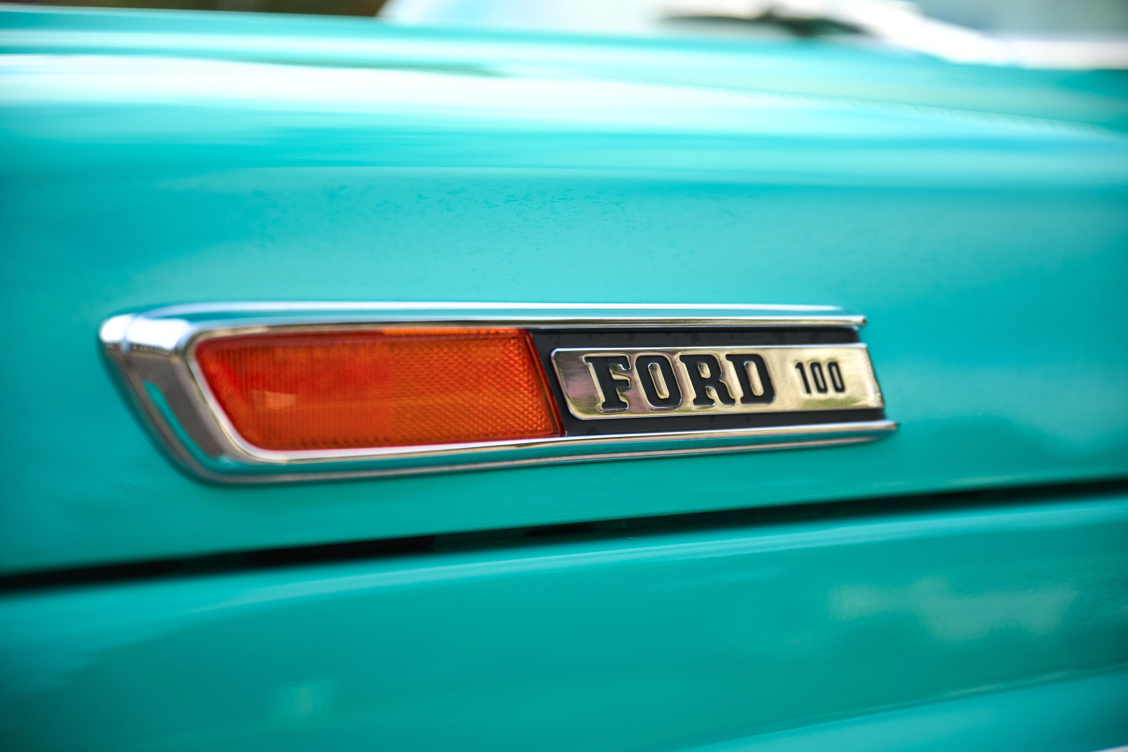 Close detail of the FORD 100 badge and amber indicator on a teal truck wing — Automotive photography, Austin A close detail of the FORD 100 badge and amber indicator on a teal truck wing.