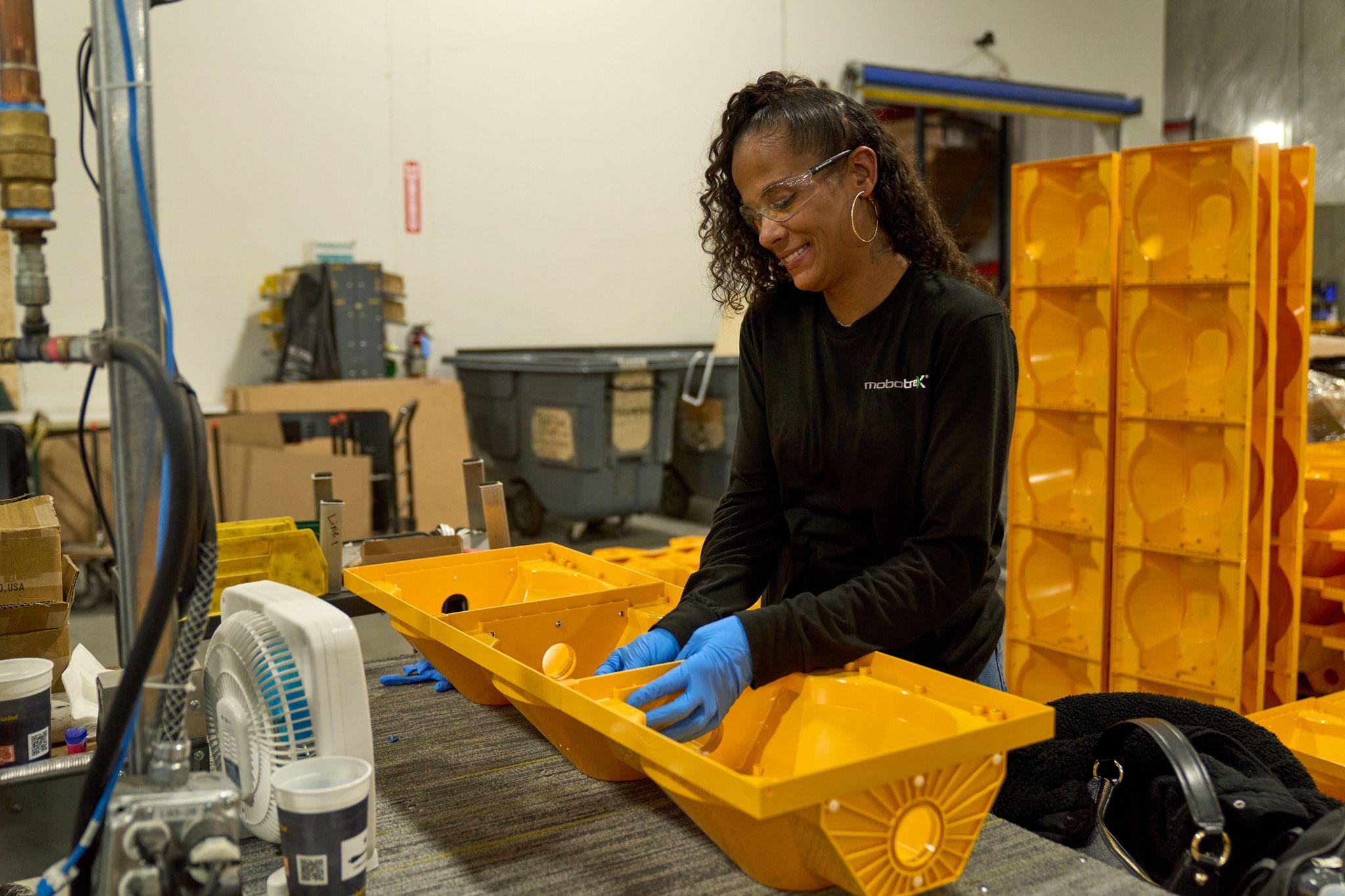 Worker in safety glasses and gloves inspecting a yellow molded plastic tray — Industrial photography, Austin Worker in safety glasses and gloves inspecting a yellow molded plastic tray in a manufacturing bay