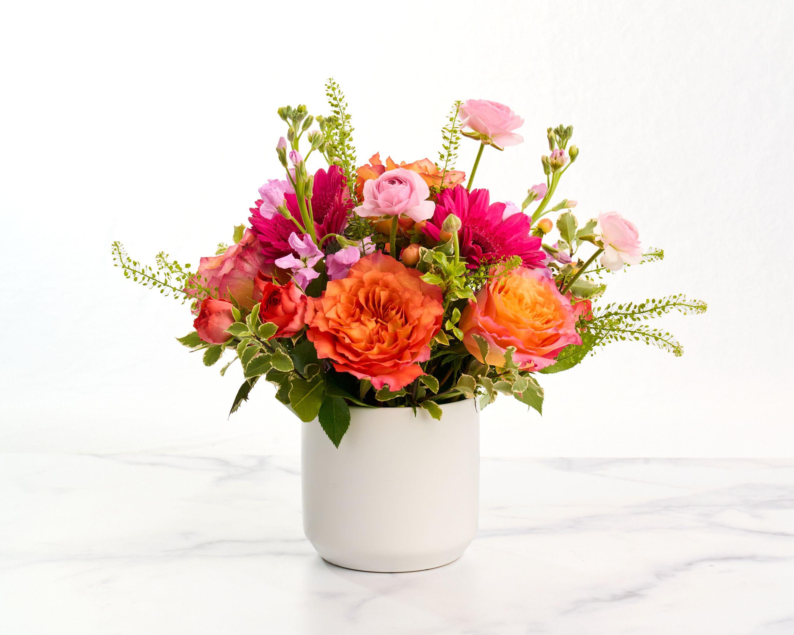 Arrangement of orange roses, pink ranunculus and greenery in a white ceramic vase — E-commerce & apparel photography, Austin Arrangement of orange roses, pink ranunculus and greenery in a white ceramic vase on white marble