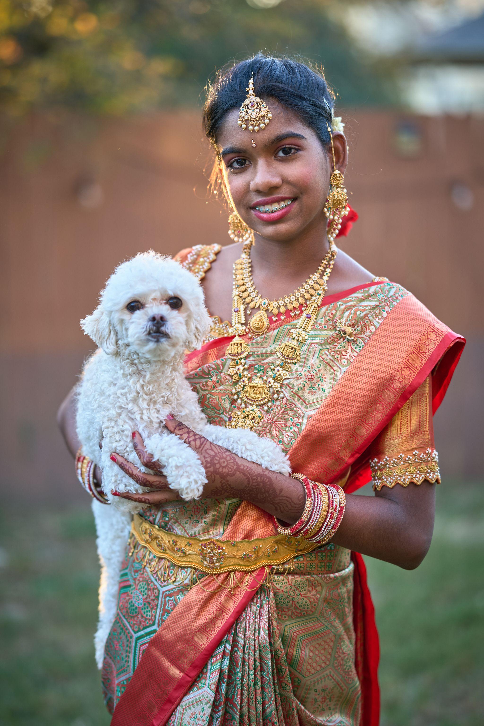 Young woman in a red and gold silk sari and temple jewelry holding a small white dog — Pet Photography photography, Austin A young woman in a red and gold silk sari and temple jewelry holding a small white dog.