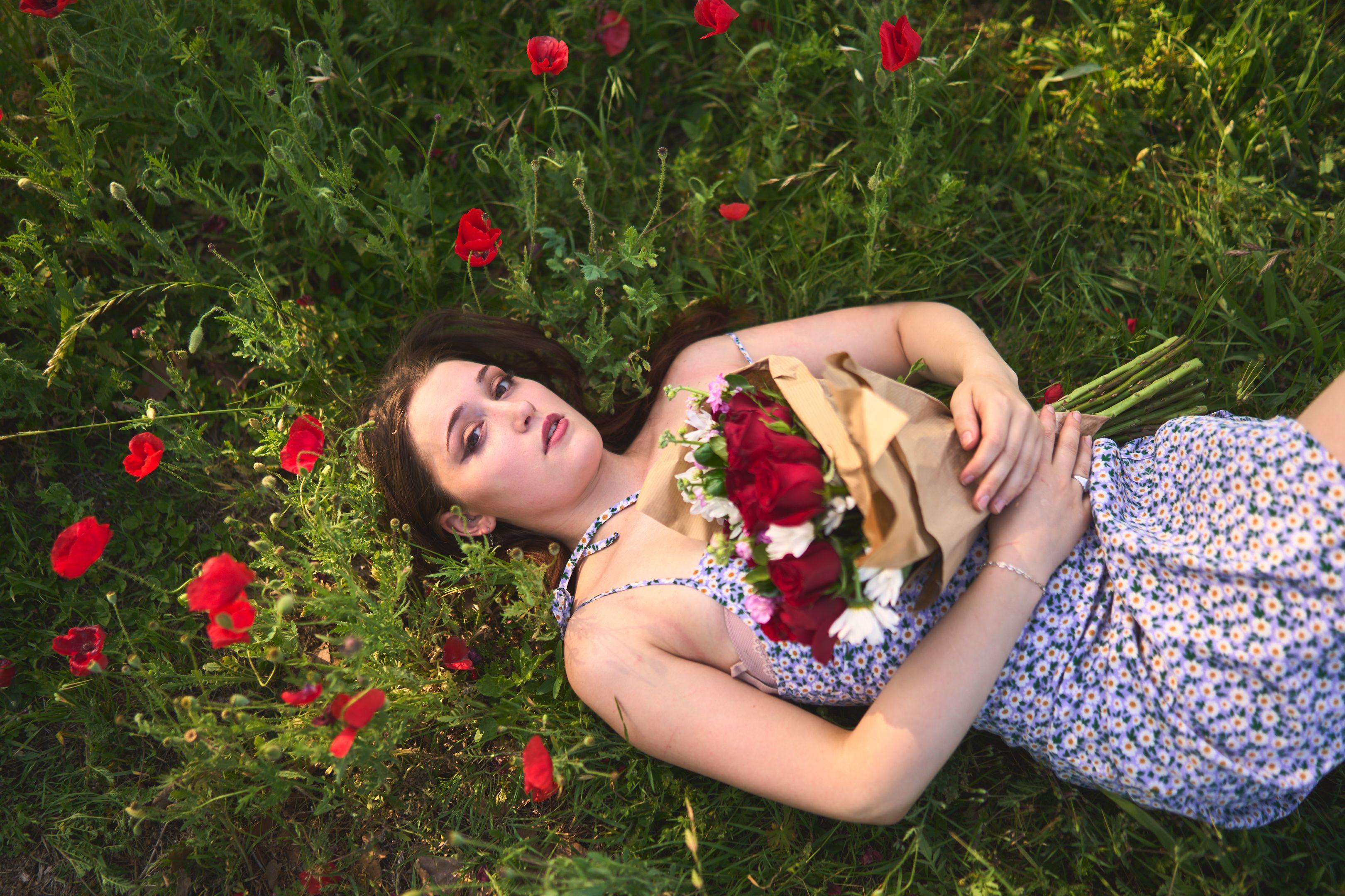Model in a blue floral dress lying in a field of grass and red poppies — Fashion & editorial photography, Austin A model in a blue floral dress lying in a field of grass and red poppies, holding a wrapped bouquet of red roses.