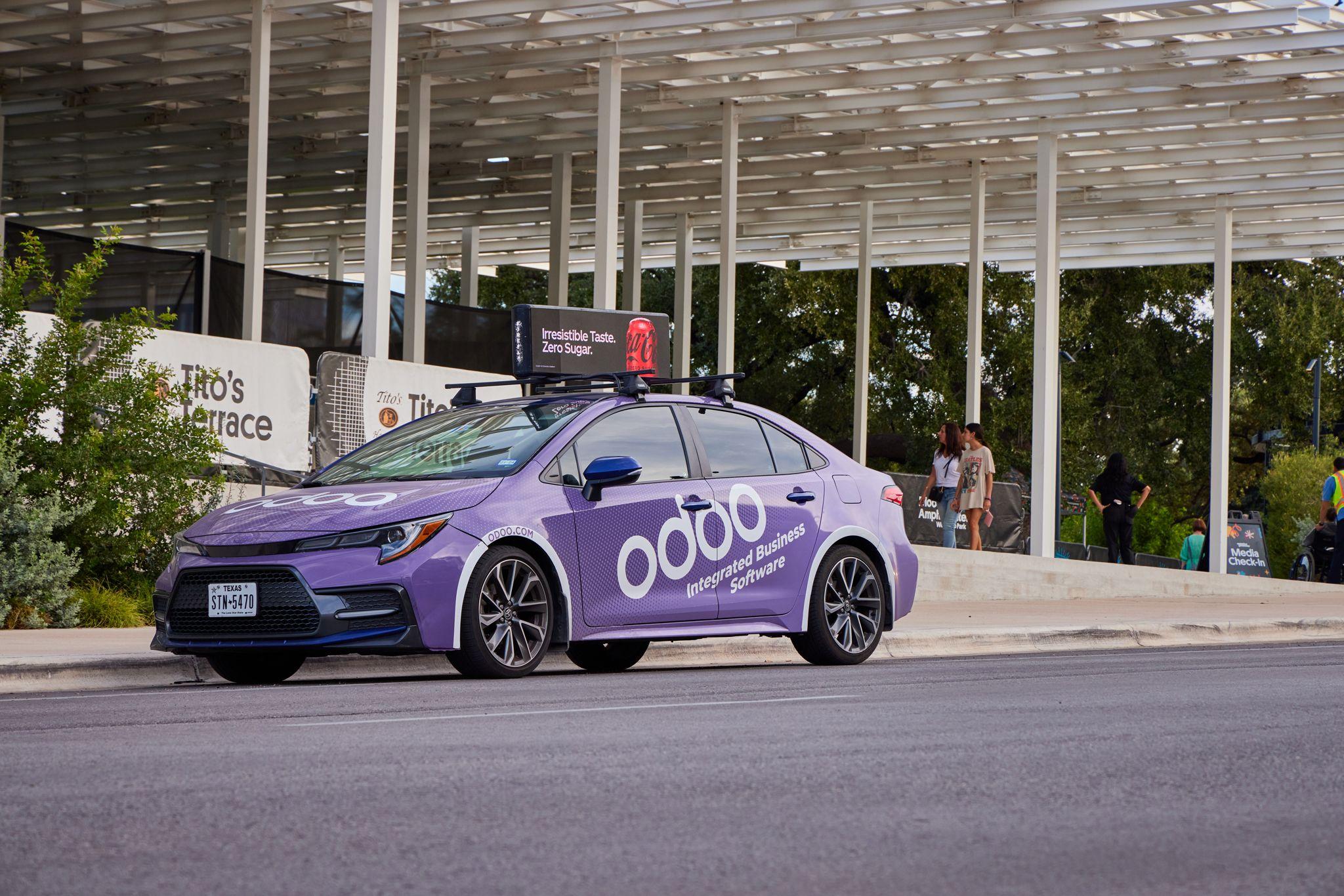 Purple Odoo-branded car with a rooftop digital screen parked outside a downtown Austin building — Downtown Austin photography, Austin A purple Odoo-branded car with a rooftop digital screen parked outside a downtown Austin building.