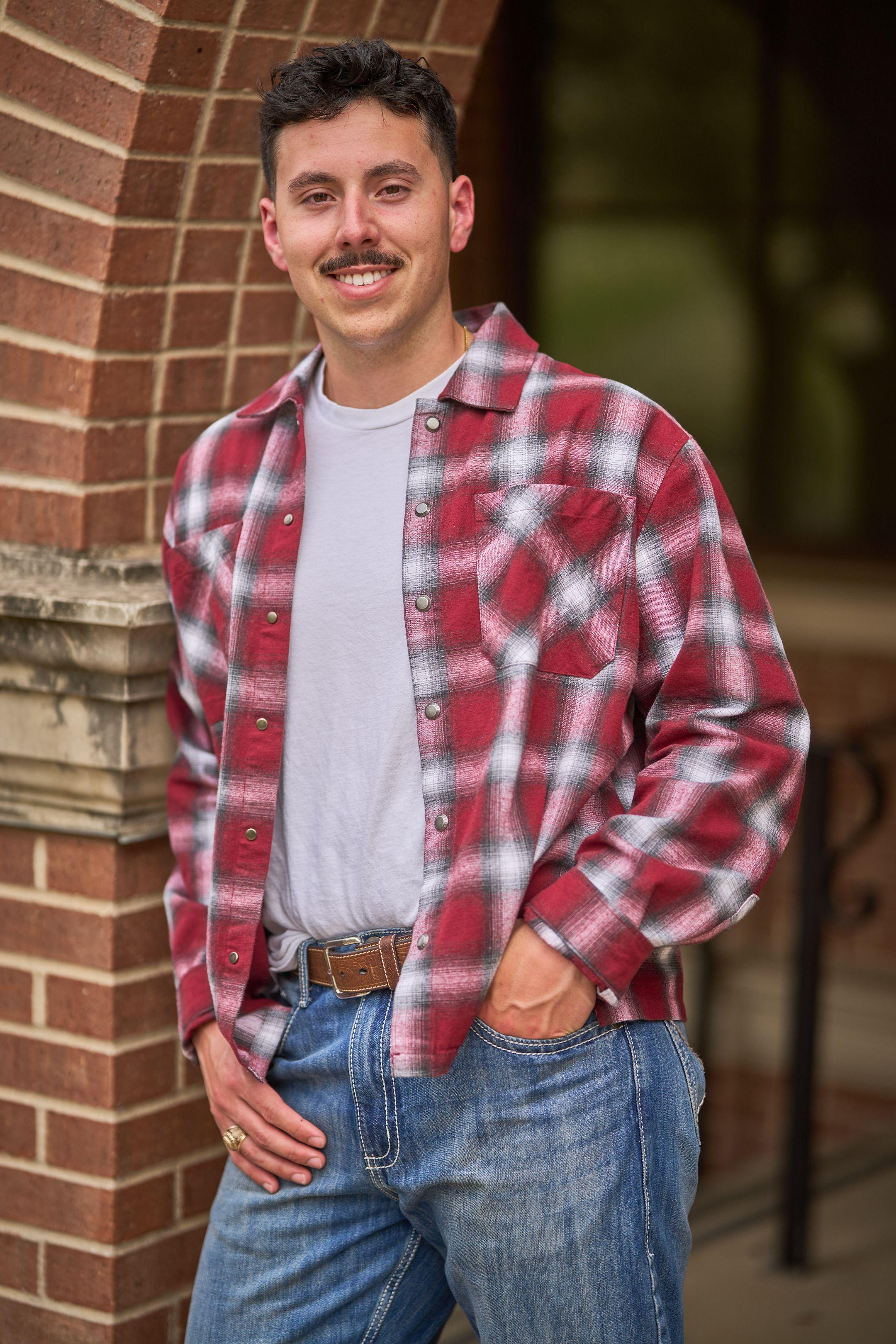 Young man in a red plaid shirt leaning against a brick wall — Headshot photography, Austin A young man in a red plaid shirt leaning against a brick wall.