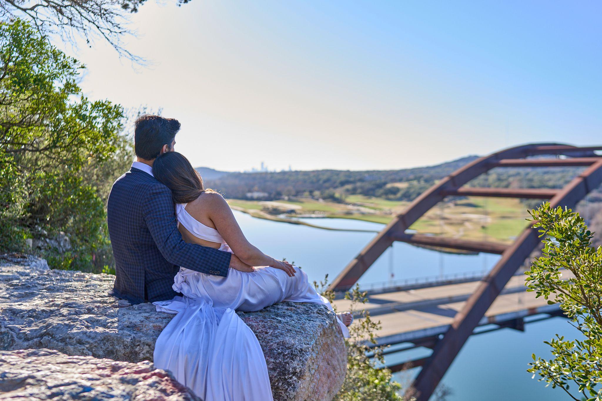 Couple sitting together on the overlook rock above Lake Austin with the Pennybacker Bridge — Pennybacker Bridge photography, Austin A couple sitting together on the overlook rock above Lake Austin with the Pennybacker Bridge in the distance