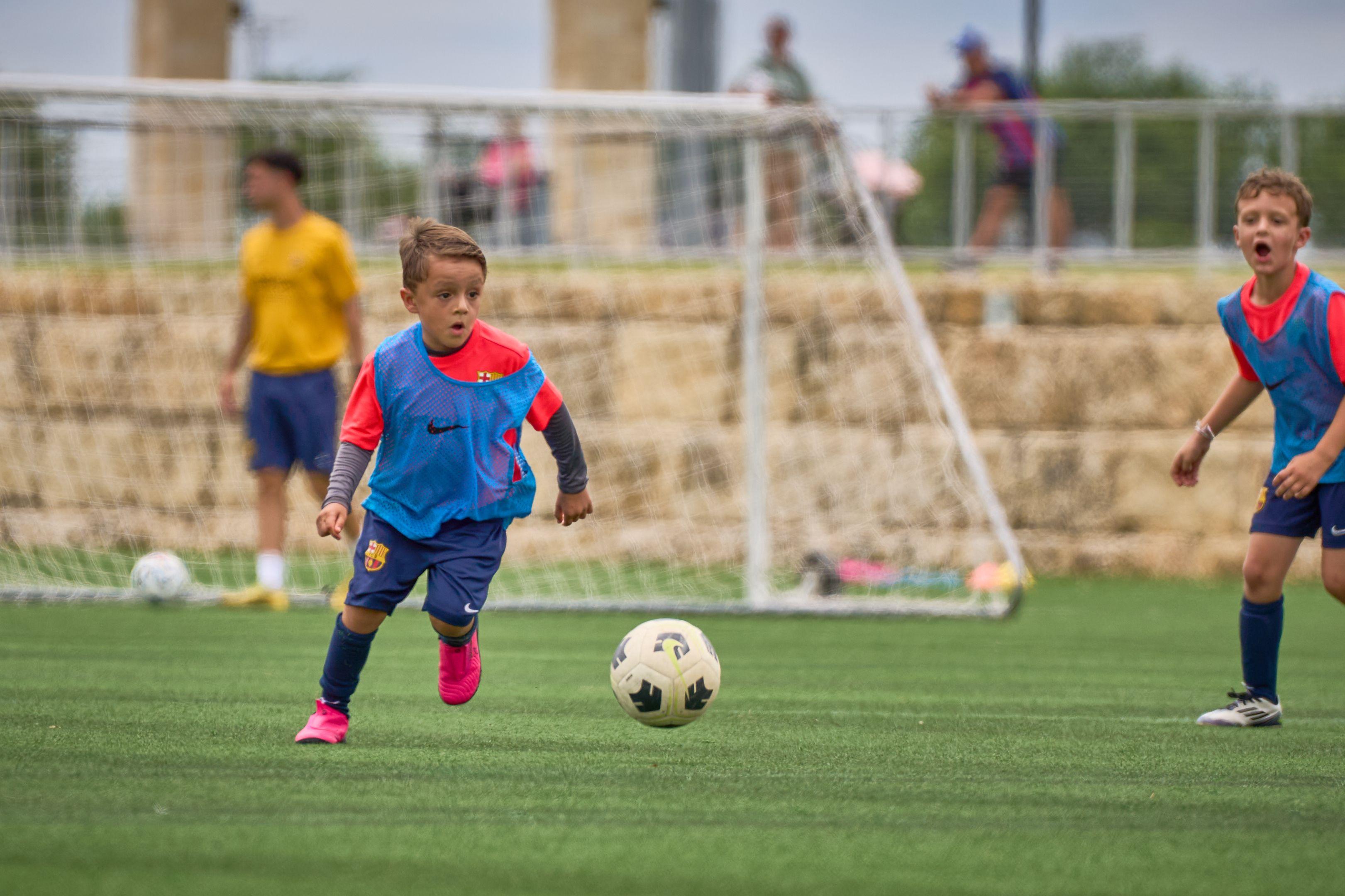 Young child in a Barcelona kit running with the ball on a pitch — School event photography, Austin Young child in a Barcelona kit running with the ball on a pitch