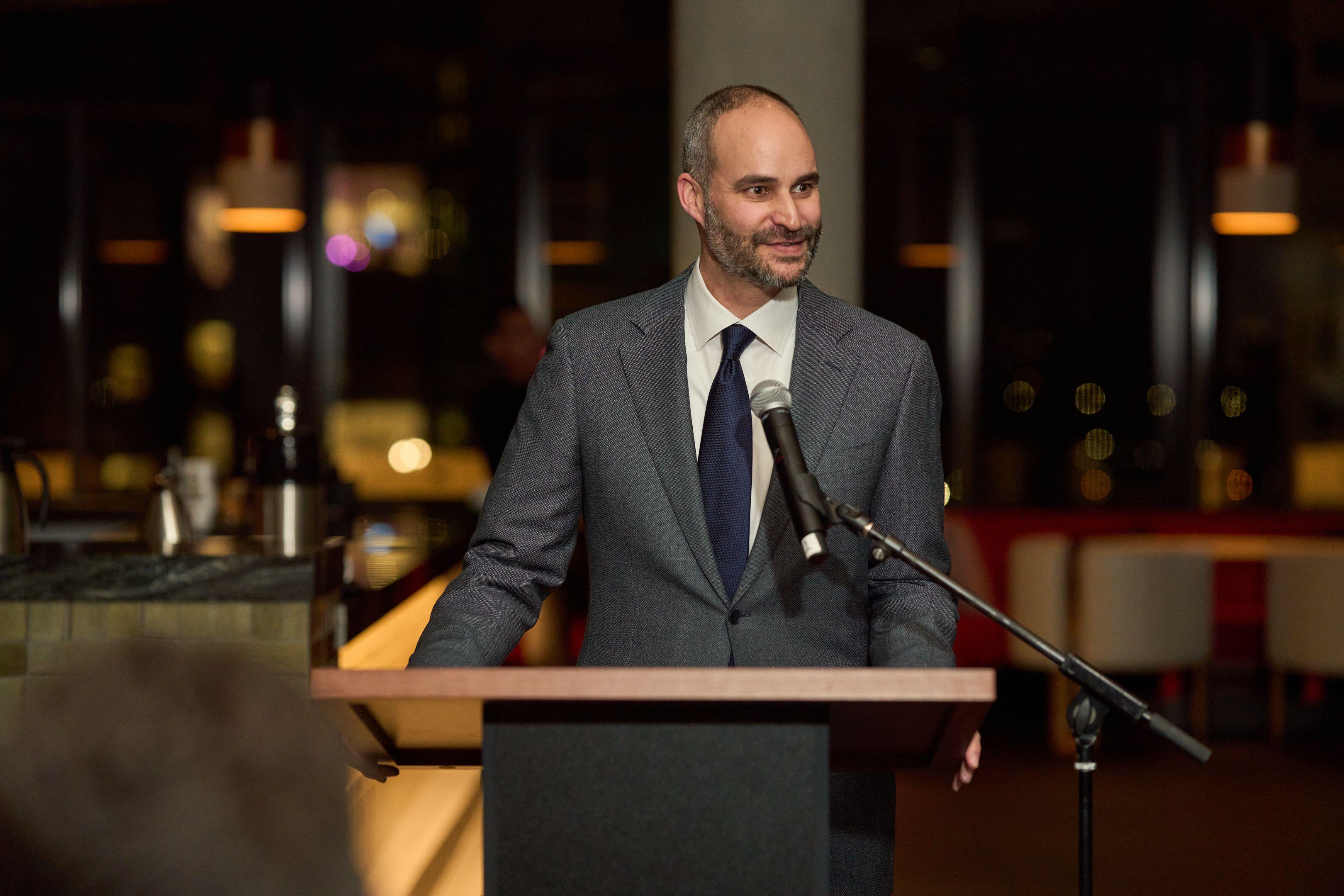 Speaker in a dark suit at a lectern microphone during an evening awards program — Business Parties photography, Austin A speaker in a dark suit at a lectern microphone during an evening awards program.