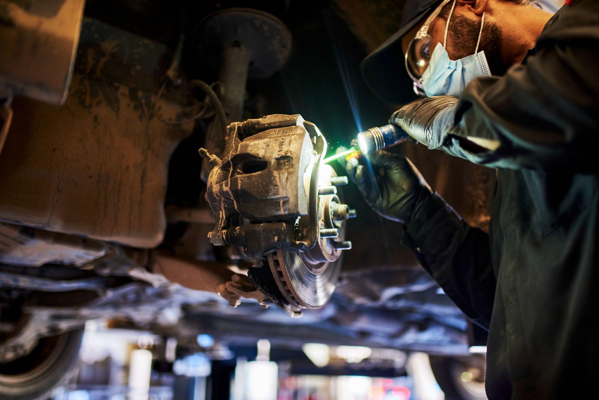 Welder in a mask cutting into a corroded component beneath a raised vehicle, sparks — Industrial photography, Austin Industrial