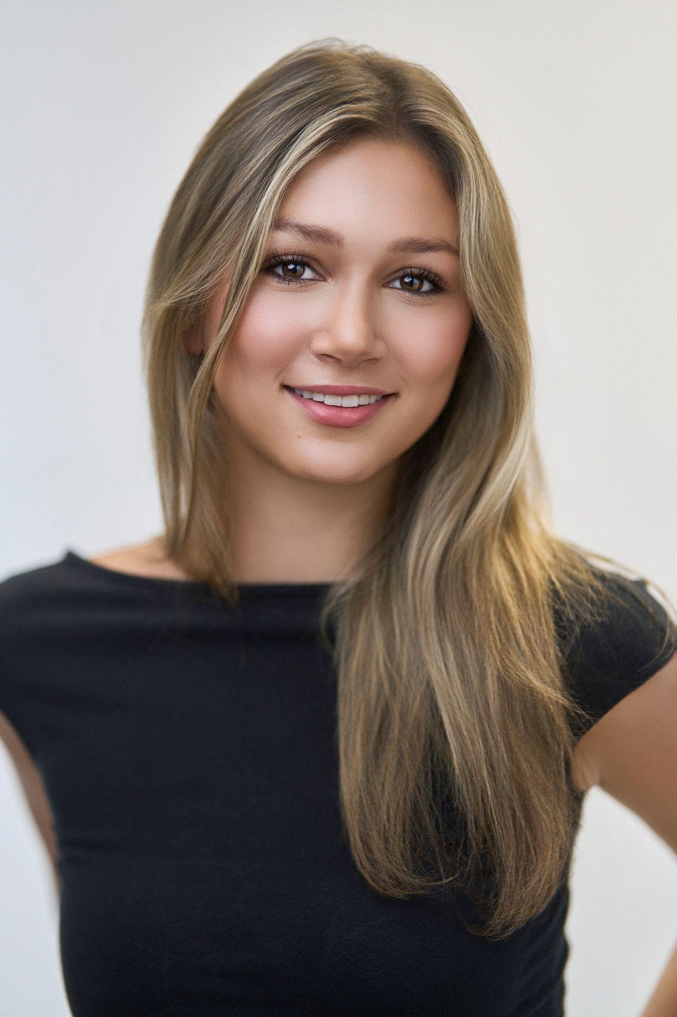 Blonde woman in a black sleeveless top smiling against a plain white studio background — Photo retouching, Austin A blonde woman in a black sleeveless top smiling against a plain white studio background.