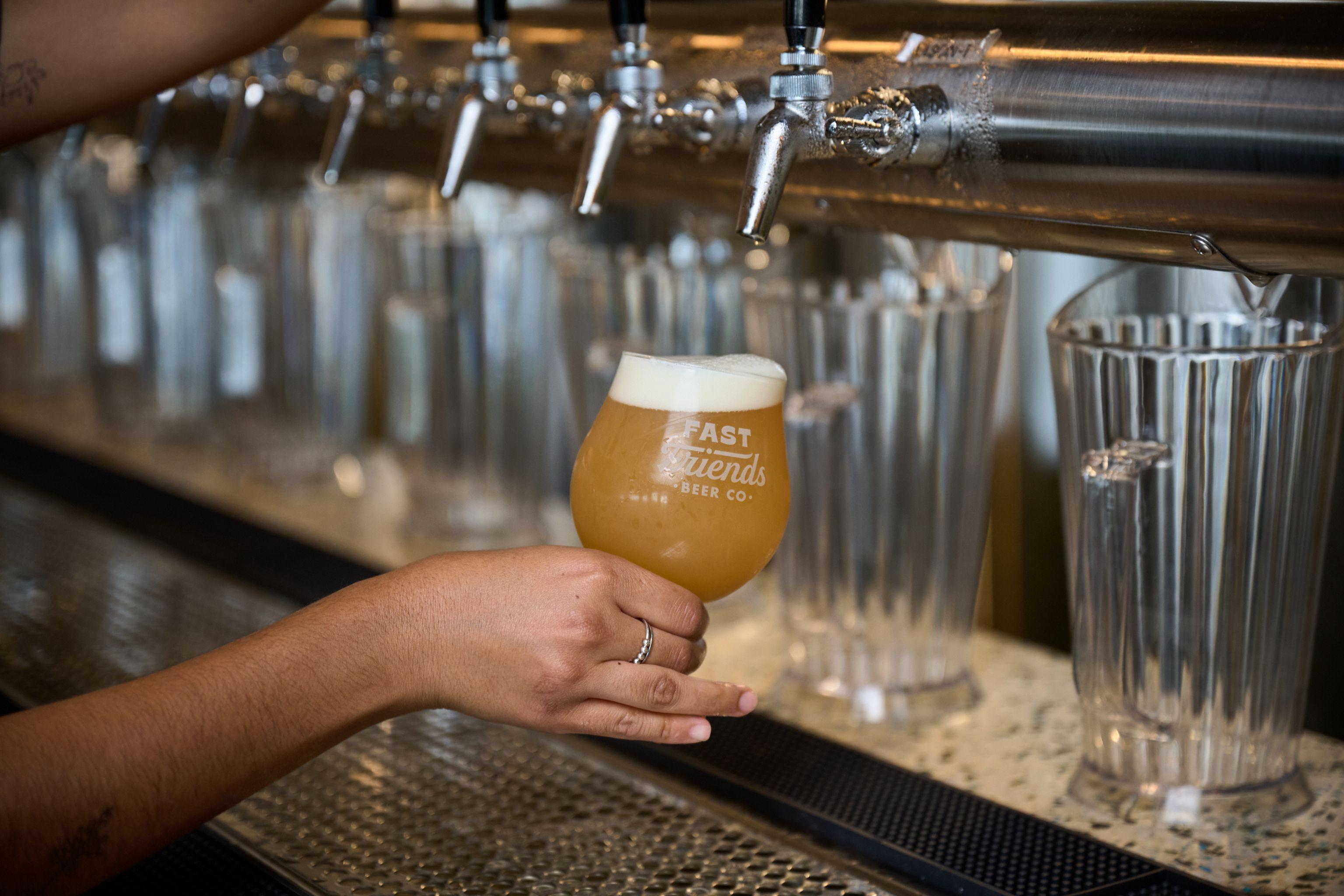 Hand holding a glass of beer beside a row of taps — Hospitality & leisure photography, Austin A hand holding a glass of beer beside a row of taps.