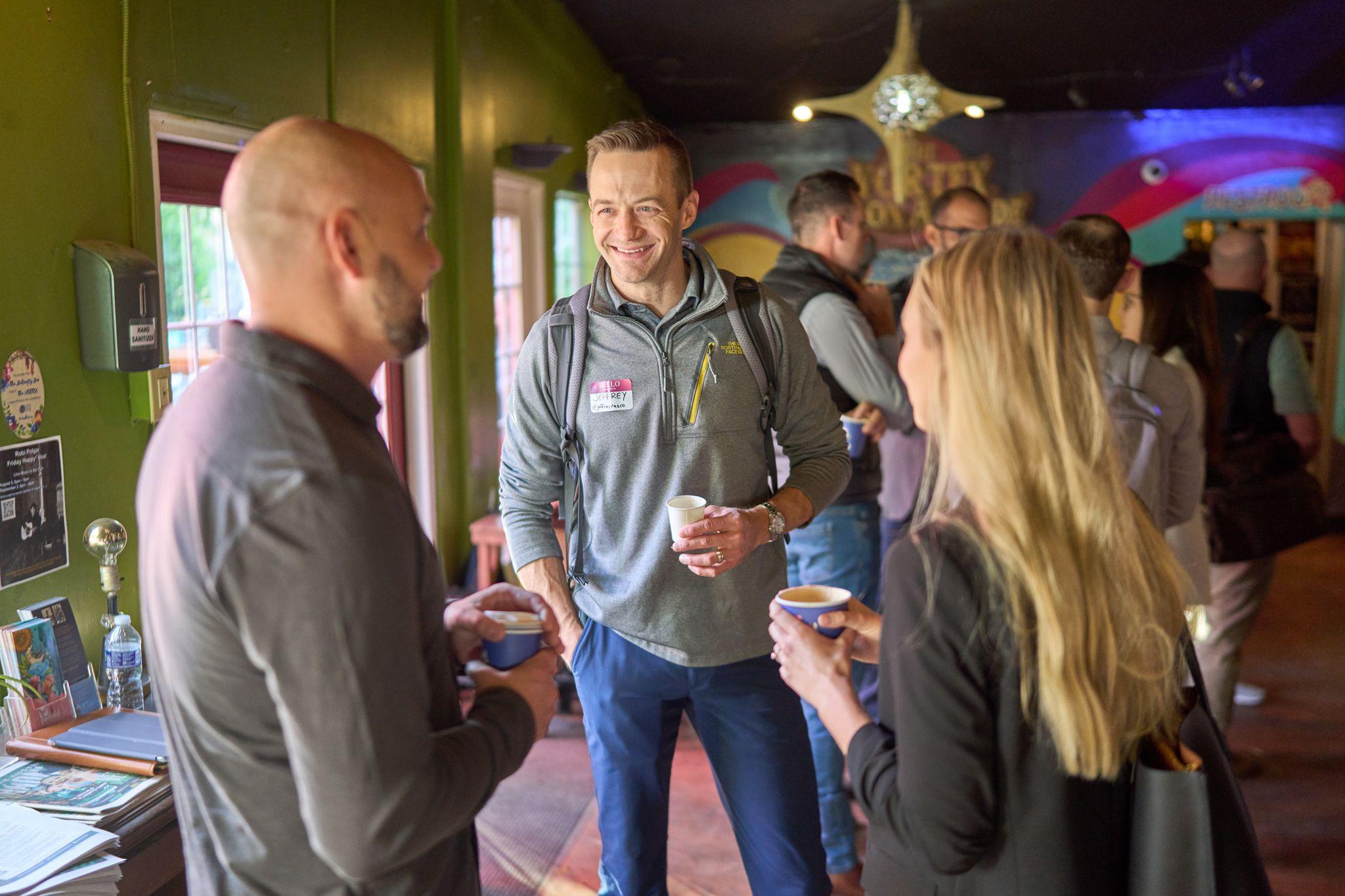 People standing with coffee cups talking at a morning networking session — Team offsite photography, Austin People standing with coffee cups talking at a morning networking session
