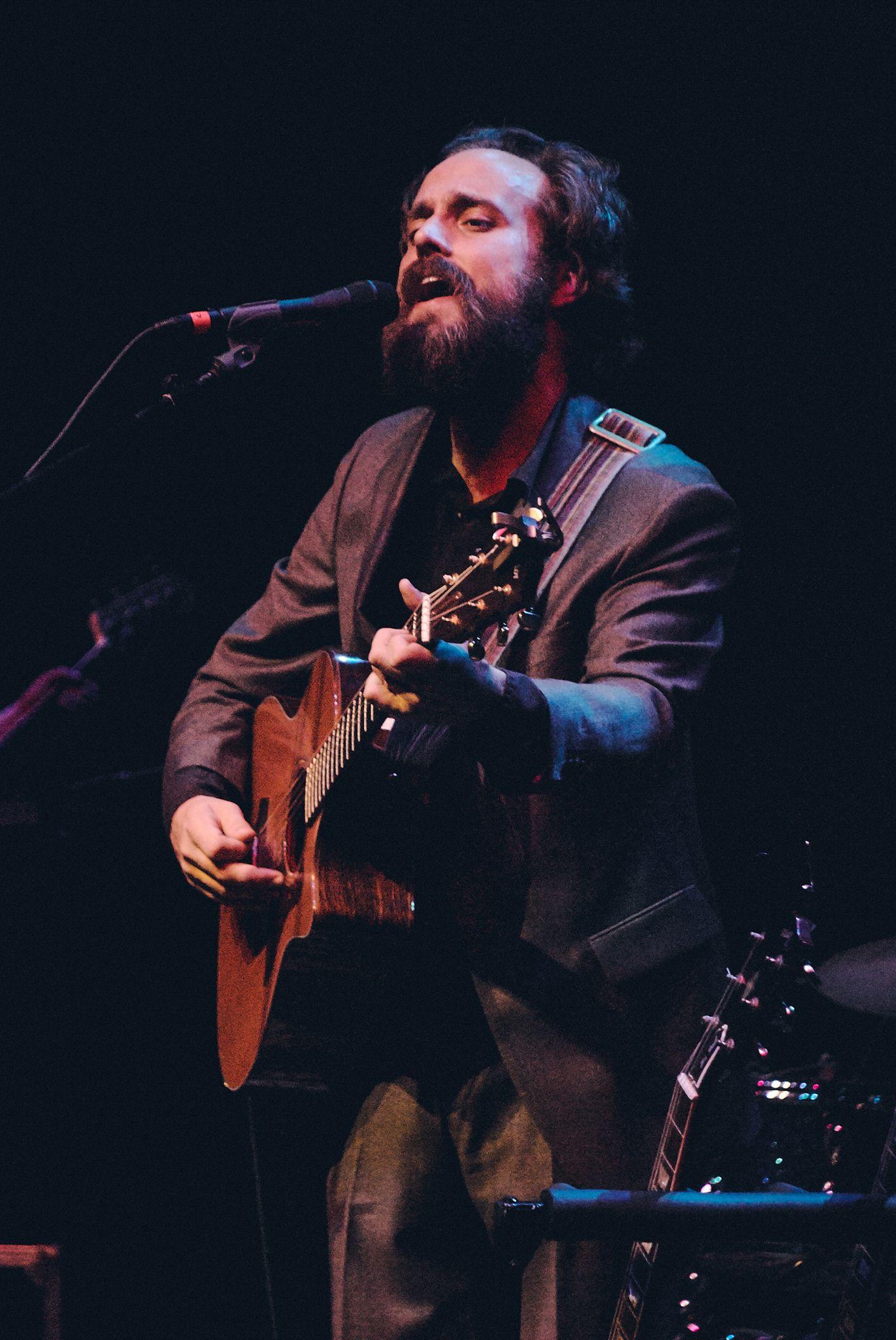 Singer playing acoustic guitar into a microphone on a dark stage — Live music photography, Austin A singer playing acoustic guitar into a microphone on a dark stage.