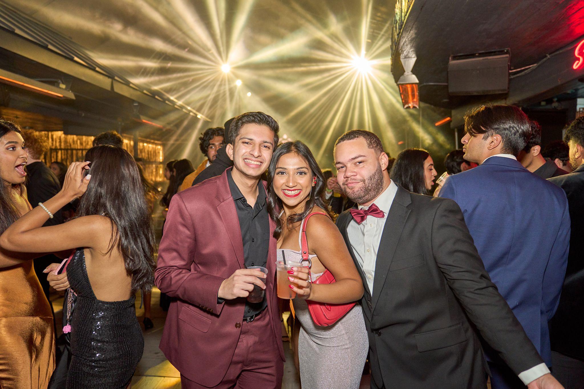 Three friends in formalwear posing with drinks under a starburst light at a party — Party & nightlife photography, Austin Party & Nightlife