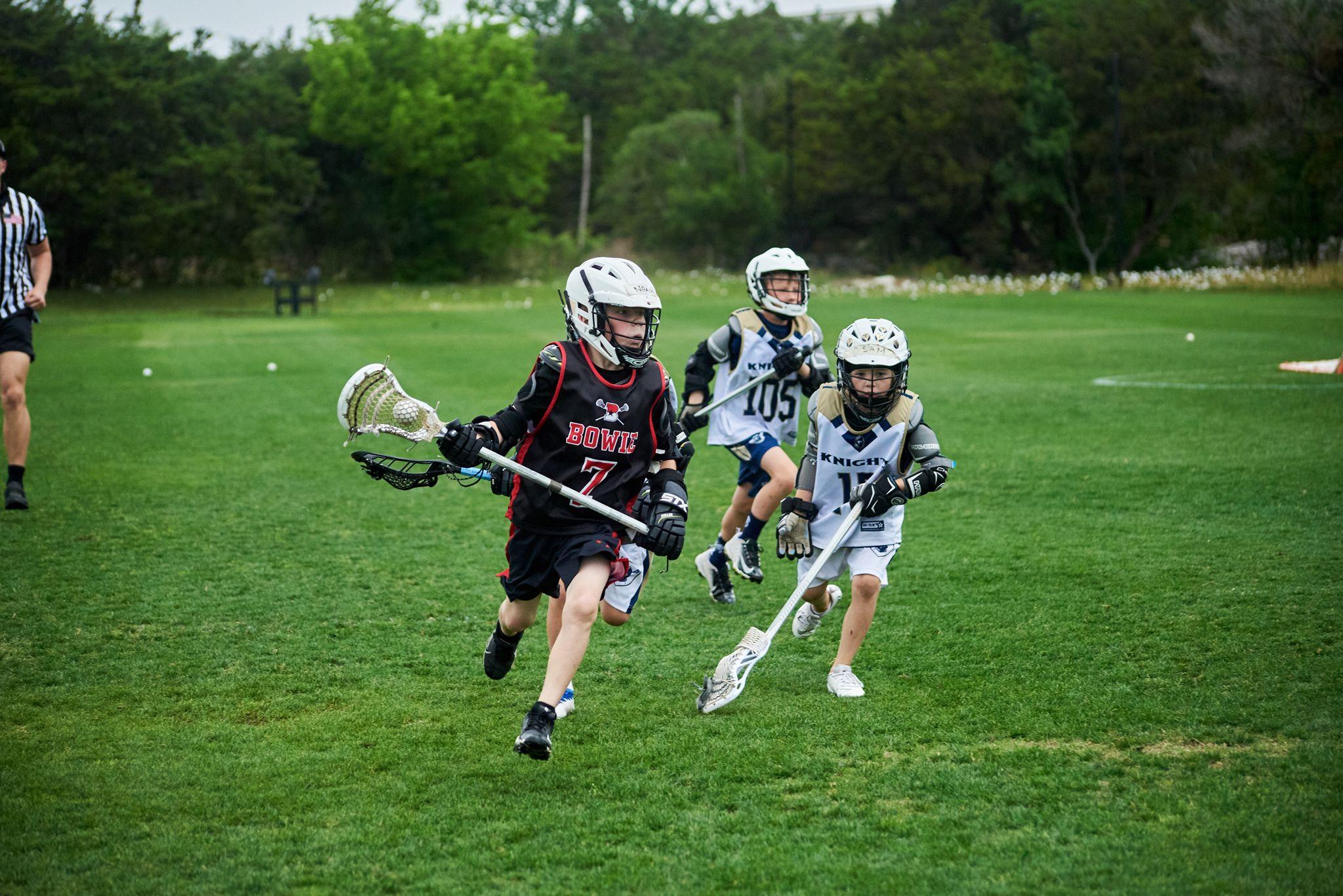 Youth lacrosse players in helmets and pads chasing a loose ball across a grass field — Sports photography, Austin Youth lacrosse players in helmets and pads chasing a loose ball across a grass field