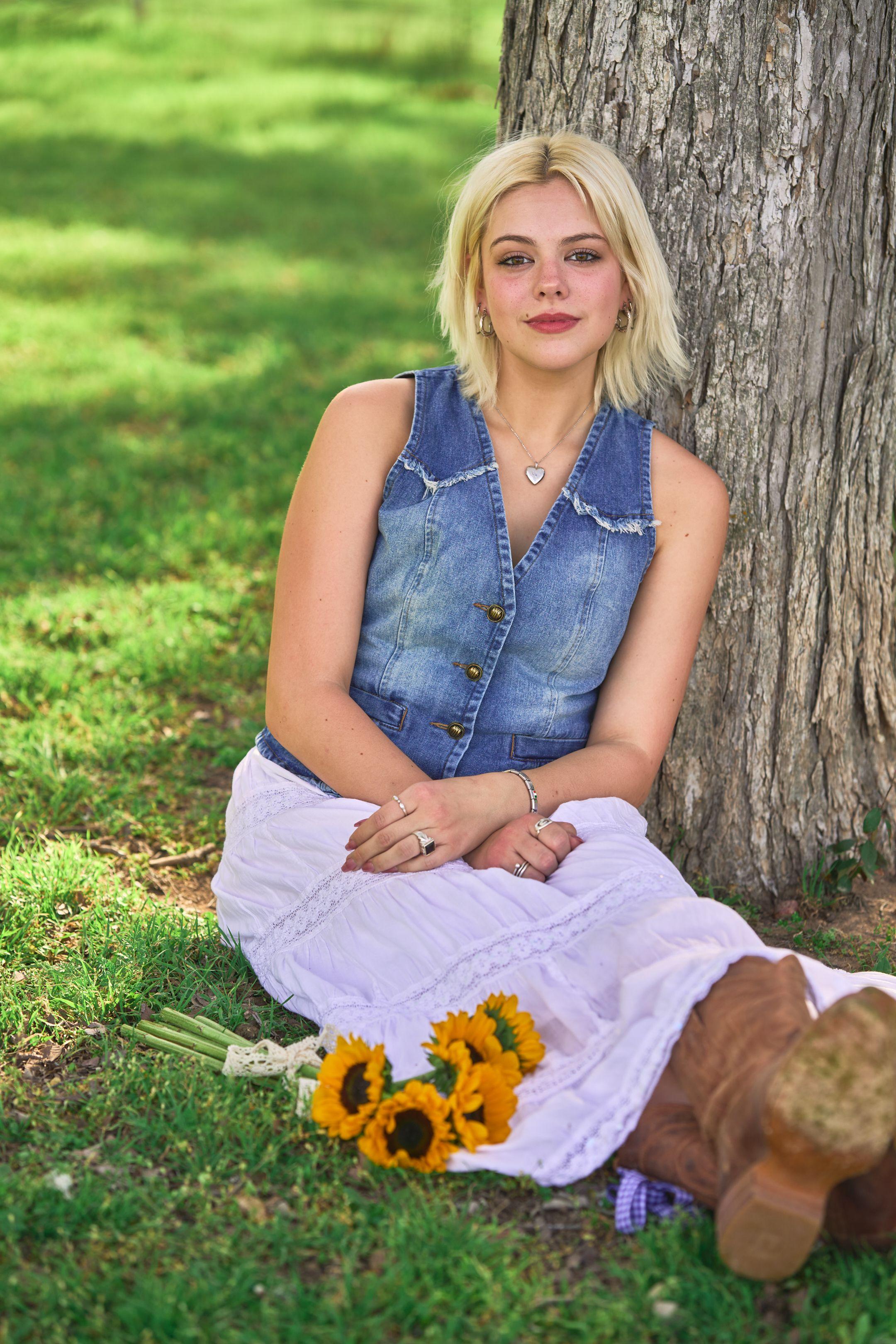 Young woman sitting against an oak trunk at Commons Ford Ranch with sunflowers in her lap — Commons Ford Ranch photography, Austin A young woman sitting against an oak trunk at Commons Ford Ranch with sunflowers in her lap