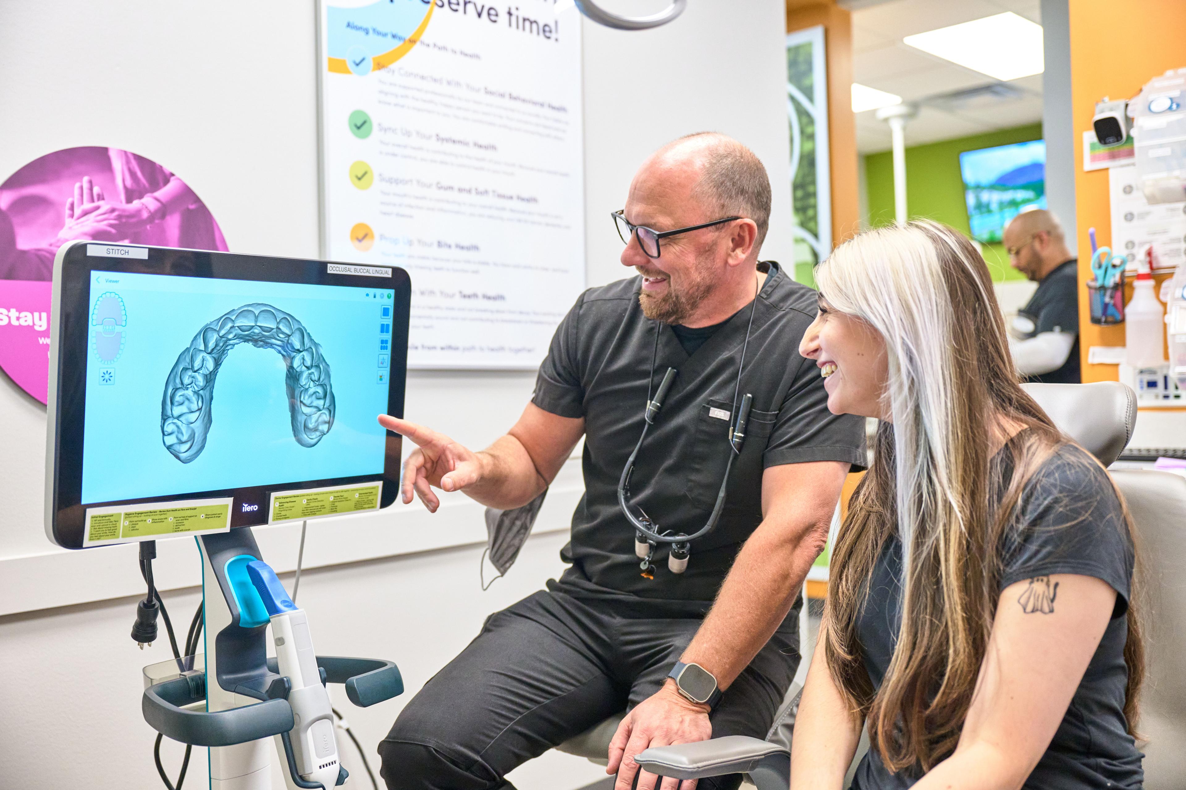 Clinician seated beside a patient pointing at a dental scan displayed on a monitor — Medical team photography, Austin Clinician seated beside a patient pointing at a dental scan displayed on a monitor