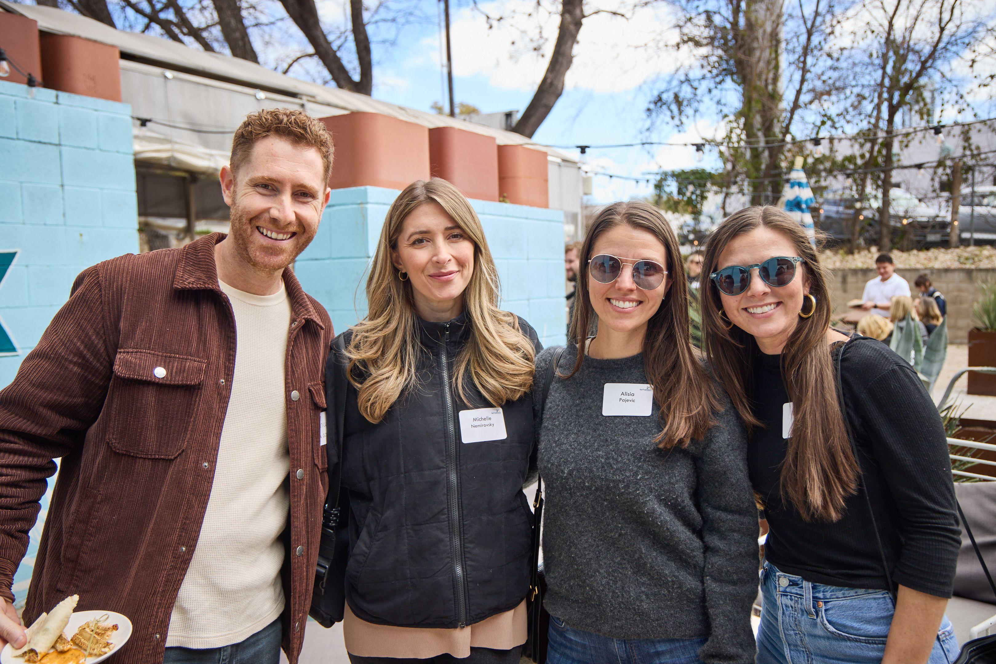 Four colleagues in fleeces and name badges posed together on an outdoor terrace at dusk — Business Parties photography, Austin Four colleagues in fleeces and name badges posed together on an outdoor terrace at dusk.