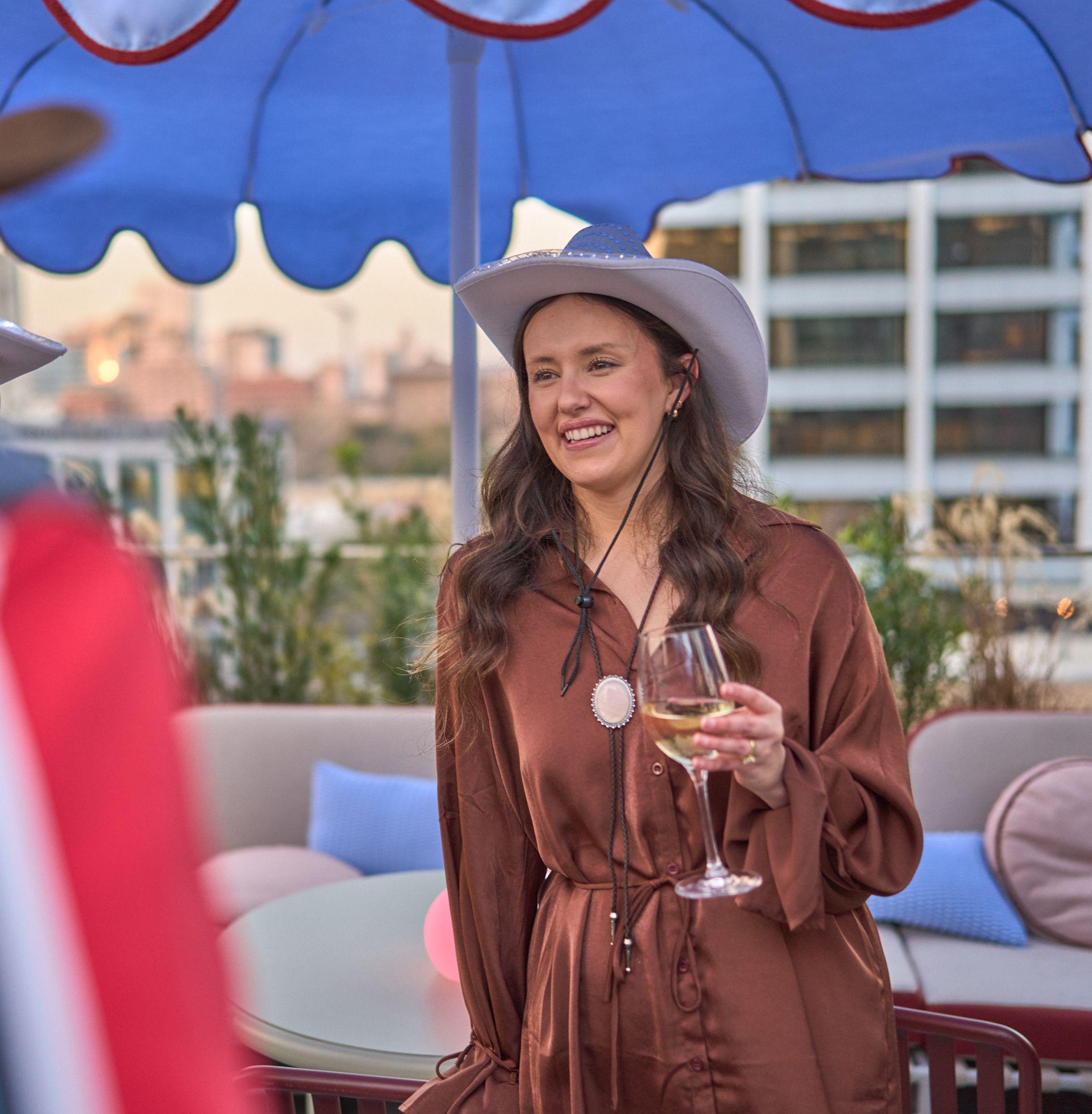 Guest in a cowboy hat holding a glass of wine on a rooftop at a western-themed party — Business Parties photography, Austin A guest in a cowboy hat holding a glass of wine on a rooftop at a western-themed party.