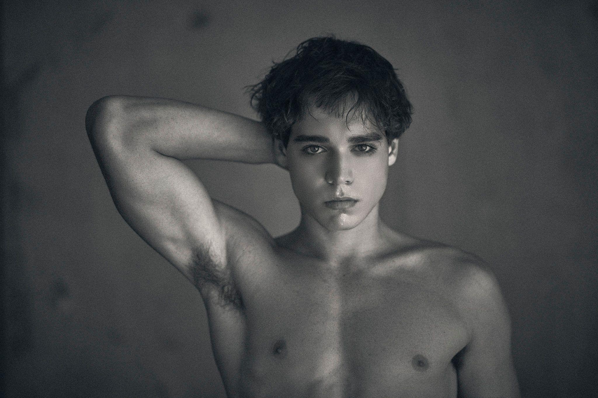 Black and white studio portrait of a shirtless male model, one arm raised behind his head — Photo retouching, Austin A black and white studio portrait of a shirtless male model, one arm raised behind his head.