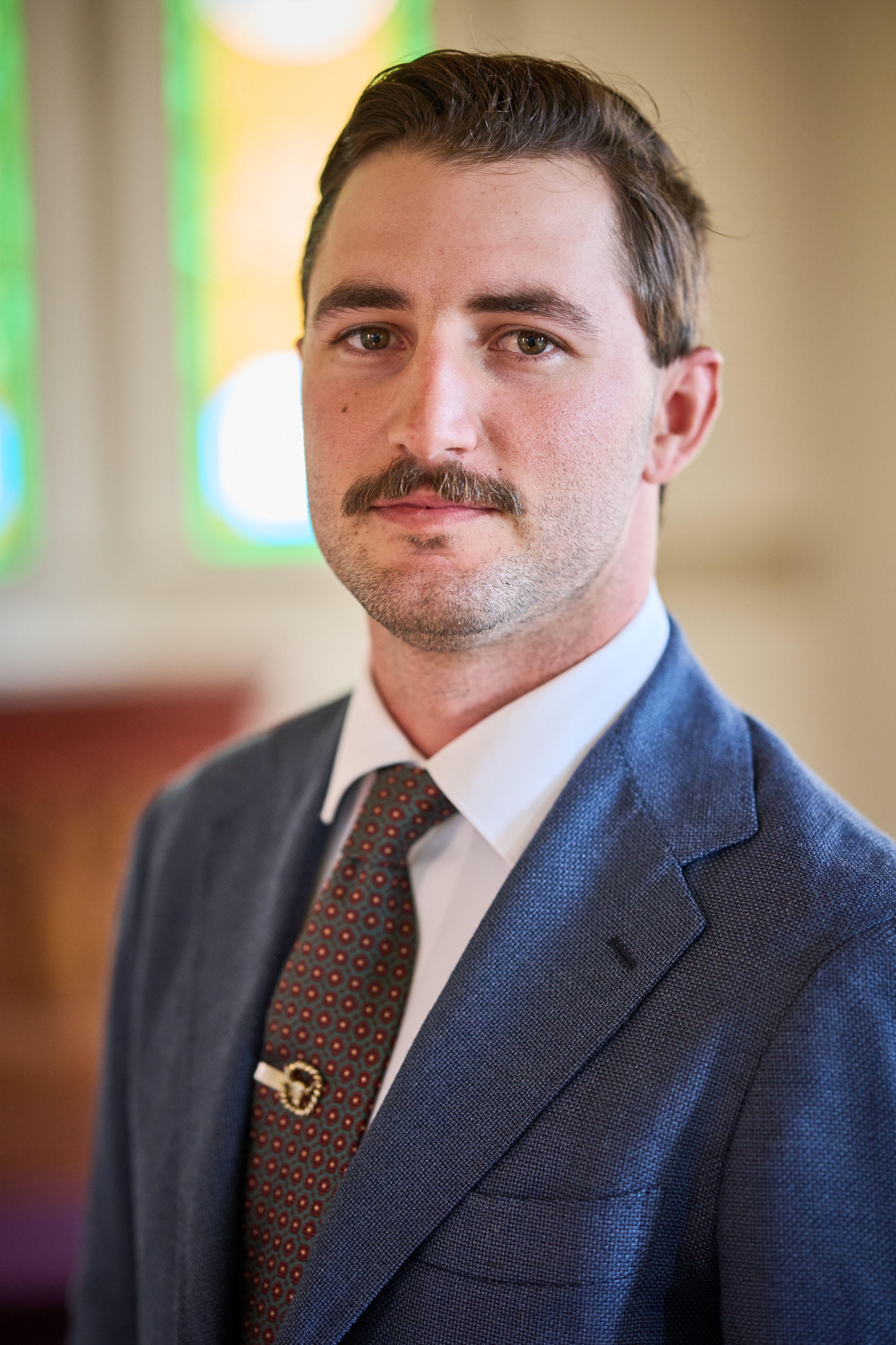 Portrait of a groom in a navy suit and brown tie in front of stained glass — Weddings photography, Austin A portrait of a groom in a navy suit and brown tie in front of stained glass.