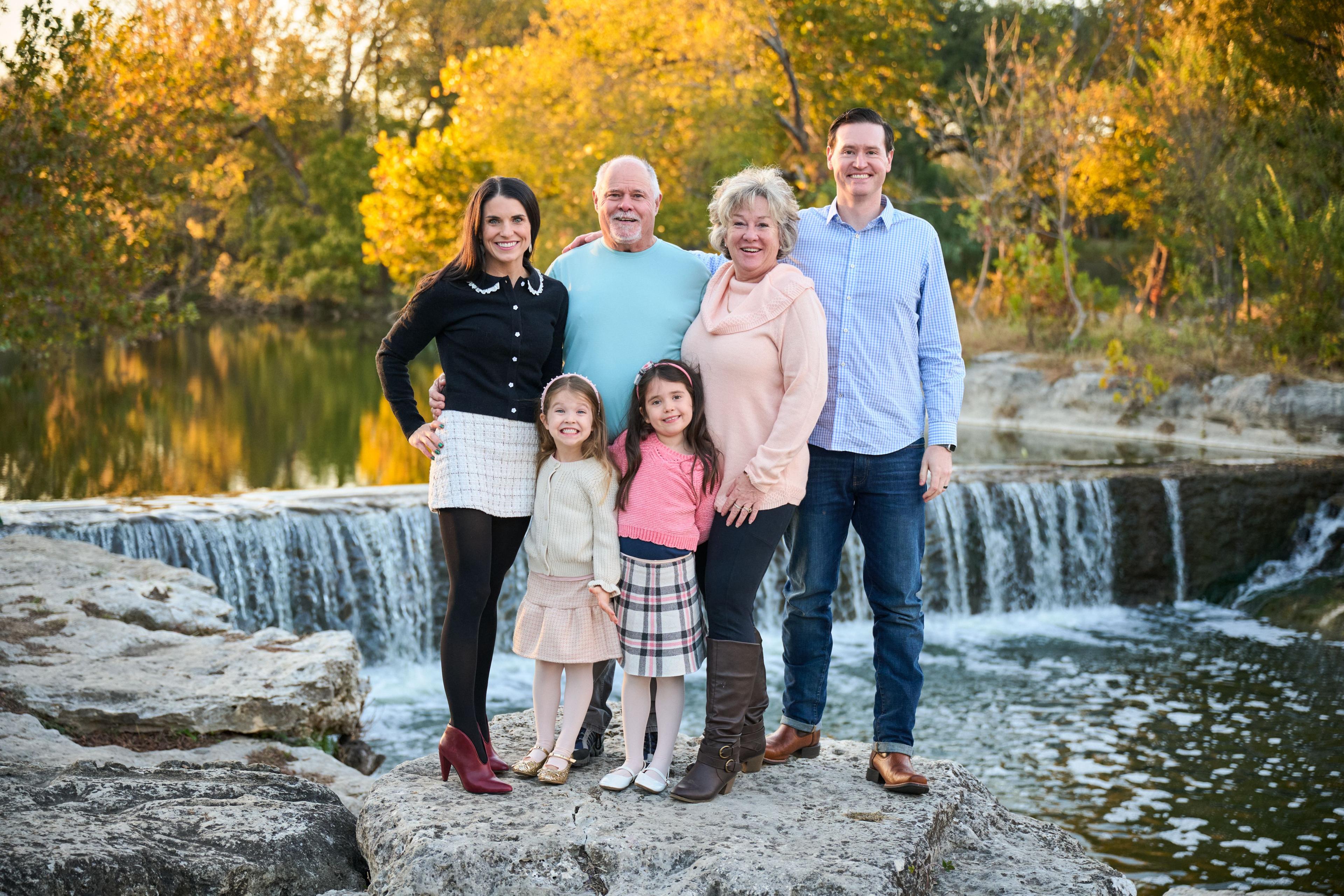 Family of six in pastels posed on the rocks in front of an autumn waterfall — Round Rock Chisholm Trail Crossing photography, Austin A family of six in pastels posed on the rocks in front of an autumn waterfall.