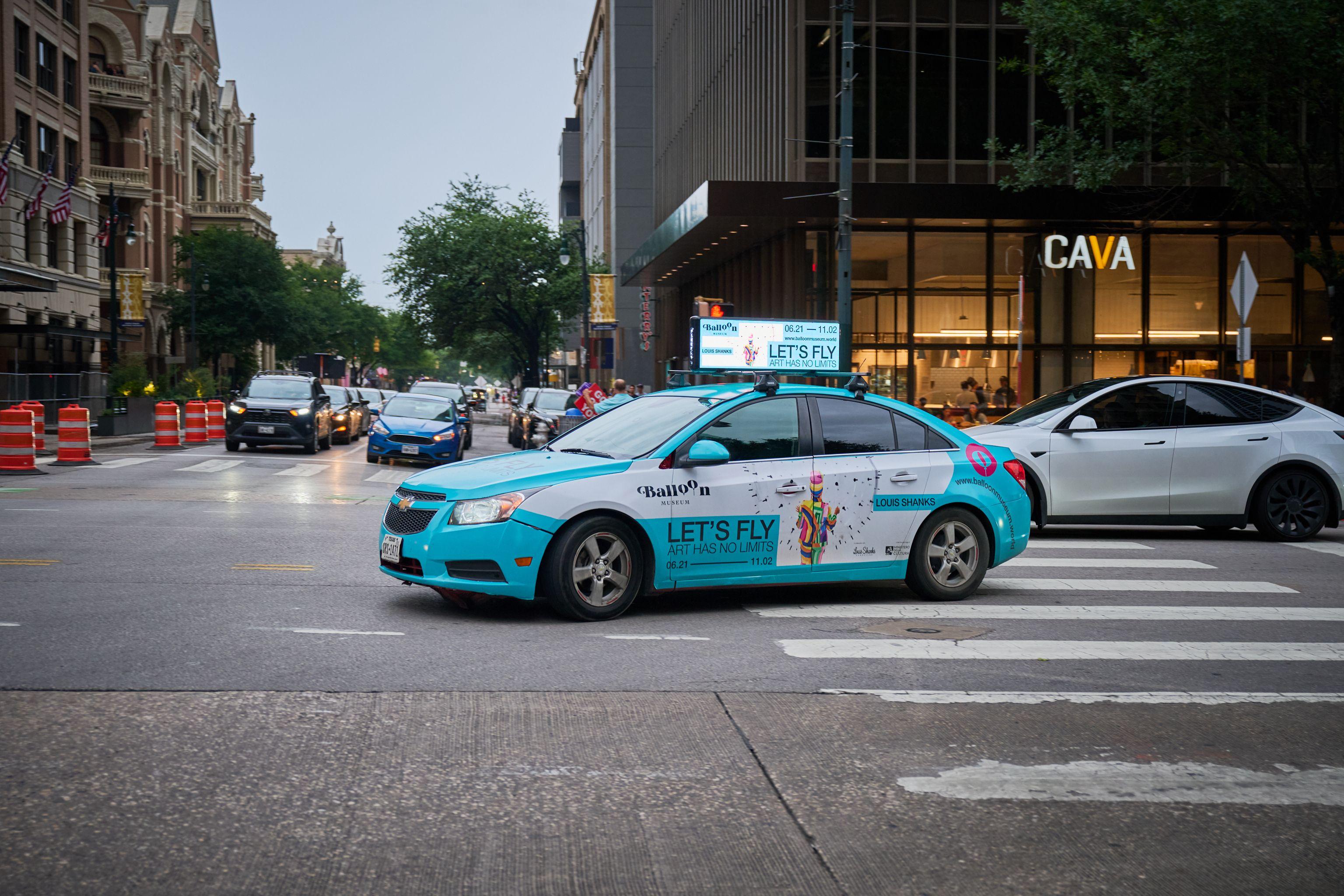Teal taxi carrying a rooftop airline ad reading 'Let's Fly' on Congress Avenue — Congress Avenue photography, Austin A teal taxi carrying a rooftop airline ad reading 'Let's Fly' on Congress Avenue.