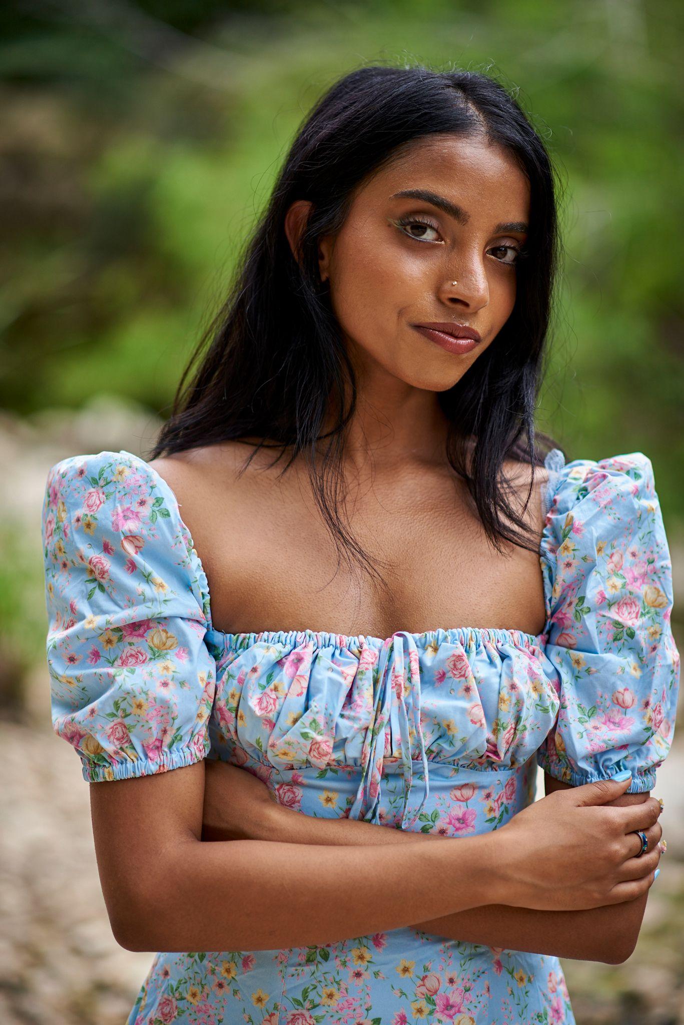Woman in a blue floral puff-sleeve top standing with arms crossed outdoors — Pease Park photography, Austin A woman in a blue floral puff-sleeve top standing with arms crossed outdoors.