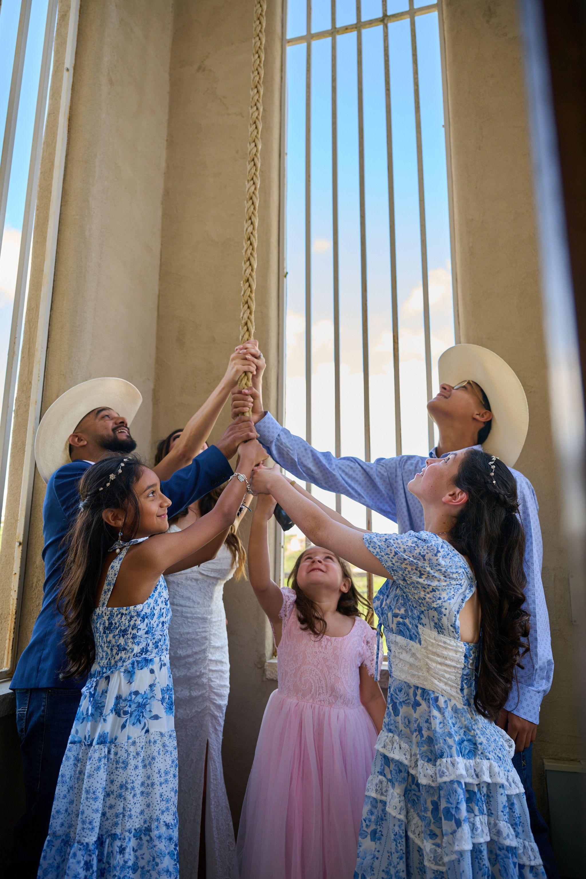 Family members in blue reaching up to ring the chapel bell together after the ceremony — Chapel Dulcinea photography, Austin Family members in blue reaching up to ring the chapel bell together after the ceremony.
