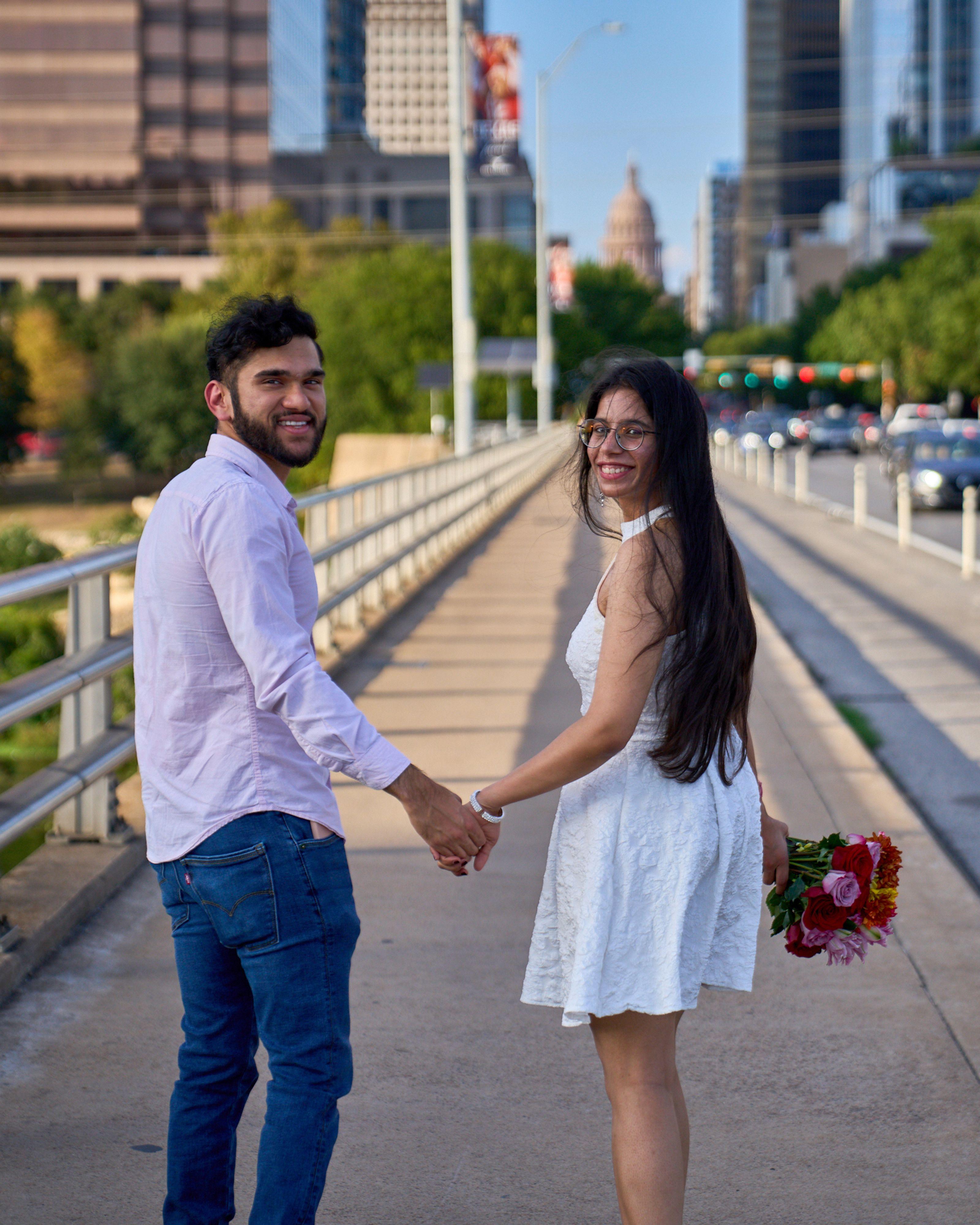 Couple holding hands on the Pfluger bridge, the Texas Capitol and downtown behind them — Congress Avenue photography, Austin A couple holding hands on the Pfluger bridge, the Texas Capitol and downtown behind them.