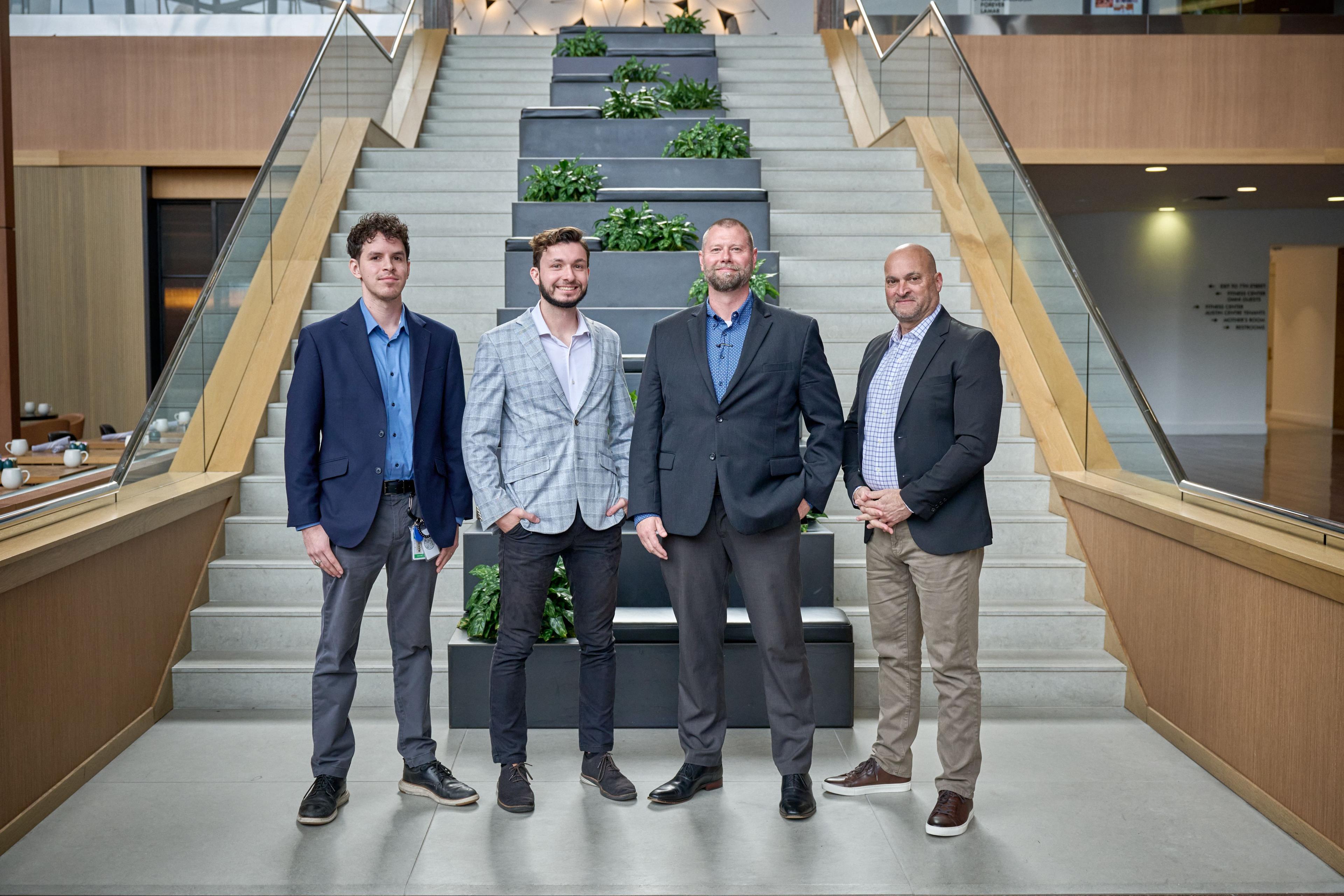 Four men in suits and blazers standing on a staircase in front of a planted green wall — Team photography, Austin Four men in suits and blazers standing on a staircase in front of a planted green wall