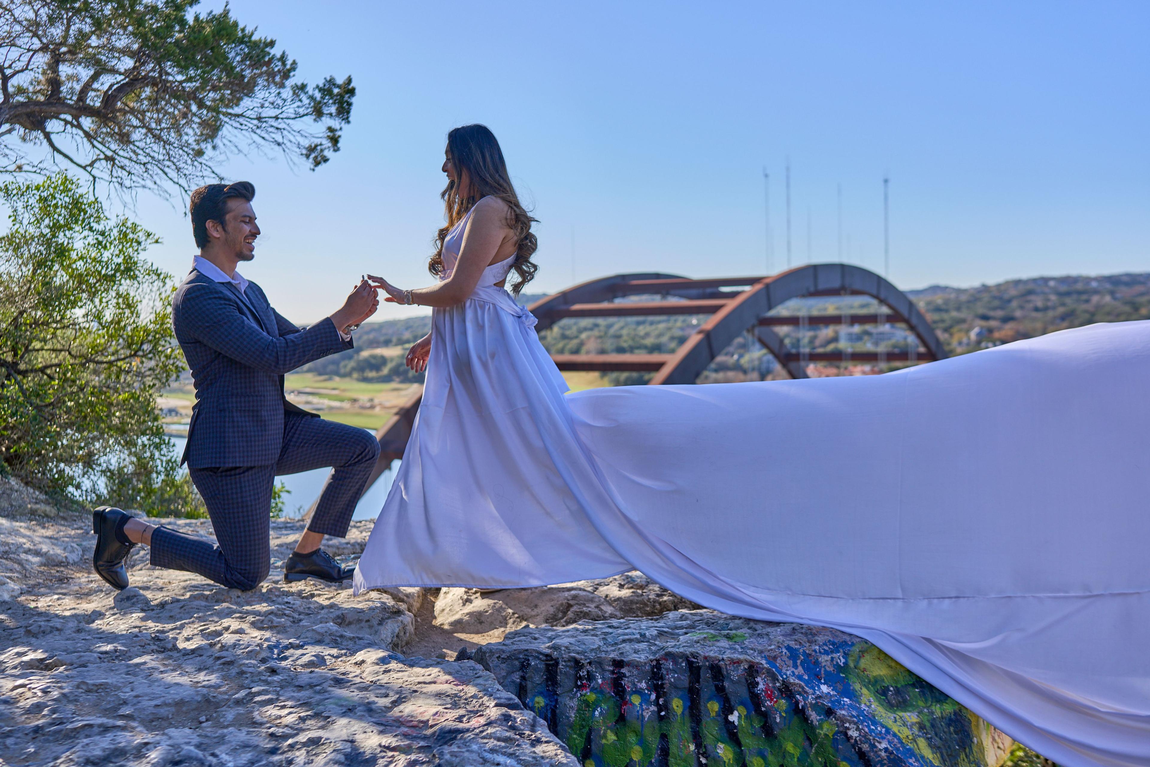 Man leading a woman by the hand across the overlook rock, her lavender dress blown out — Pennybacker Bridge photography, Austin A man leading a woman by the hand across the overlook rock, her lavender dress blown out behind her, the Pennybacker Bridge beyond