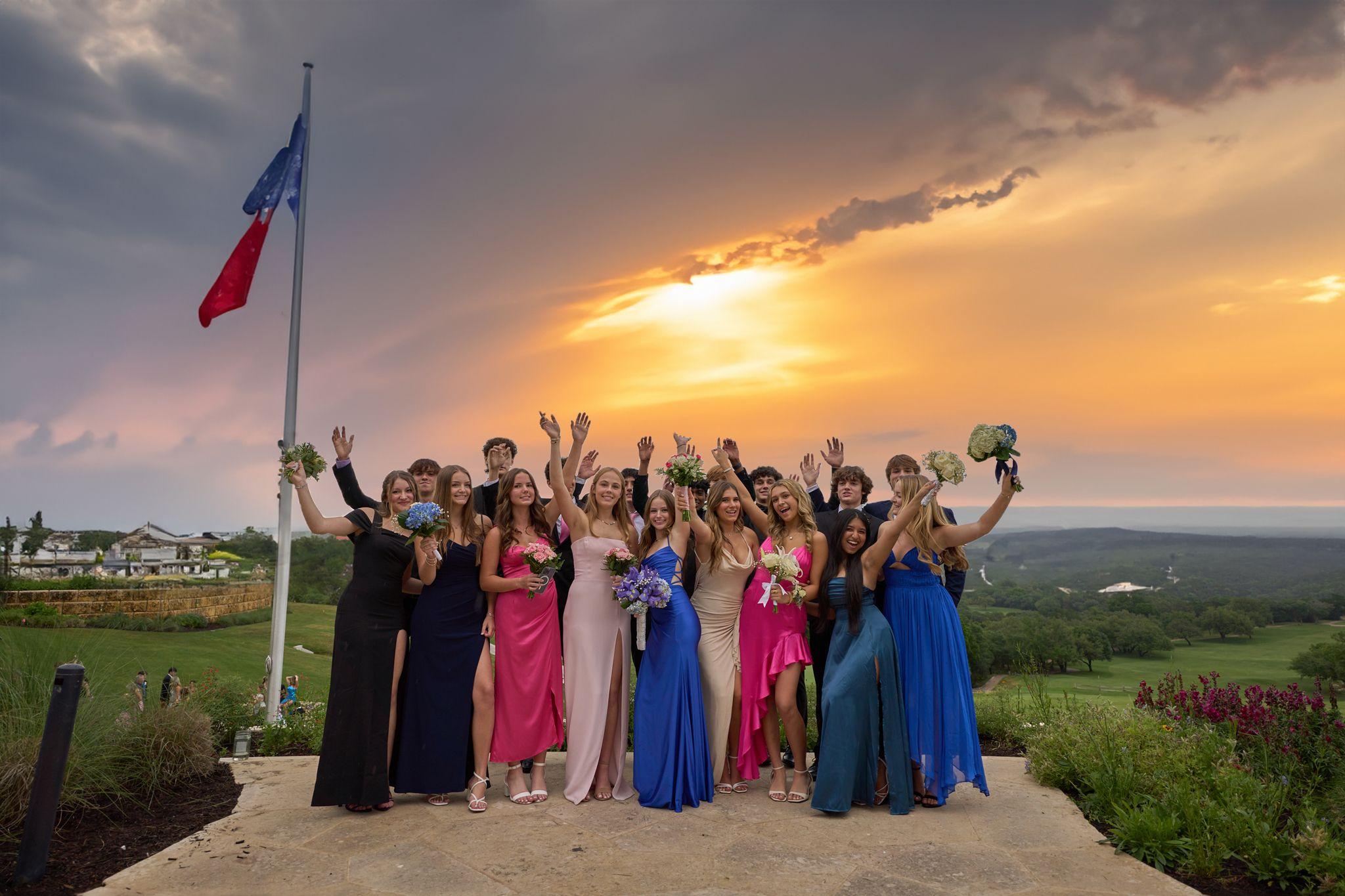 Group of prom-goers in gowns and suits cheering against a sunset sky — Graduation & Prom photography, Austin A group of prom-goers in gowns and suits cheering against a sunset sky.