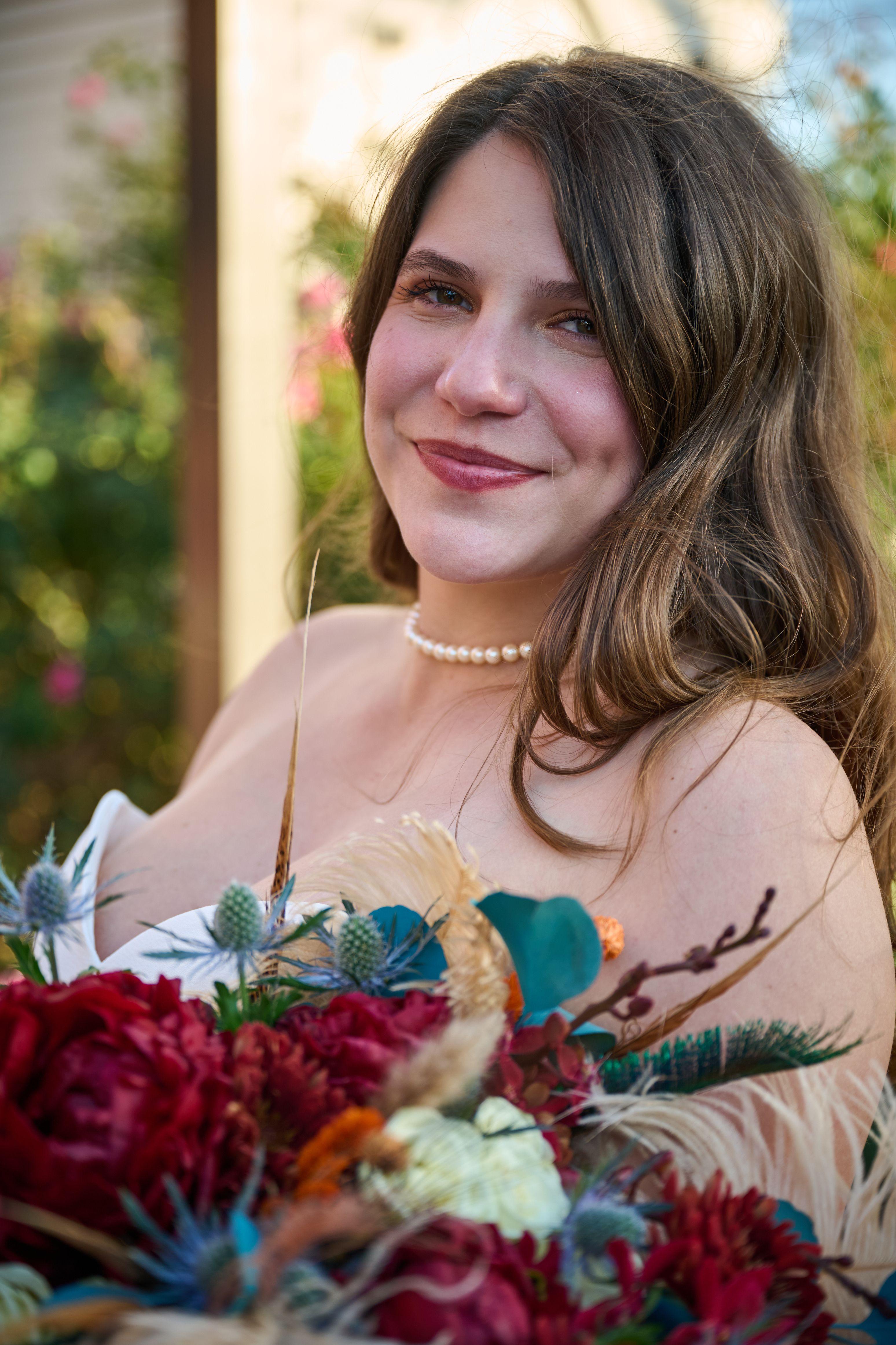 Bride smiling over her shoulder holding a red, teal and dried-grass bouquet at golden hour — Weddings photography, Austin A bride smiling over her shoulder holding a red, teal and dried-grass bouquet at golden hour.