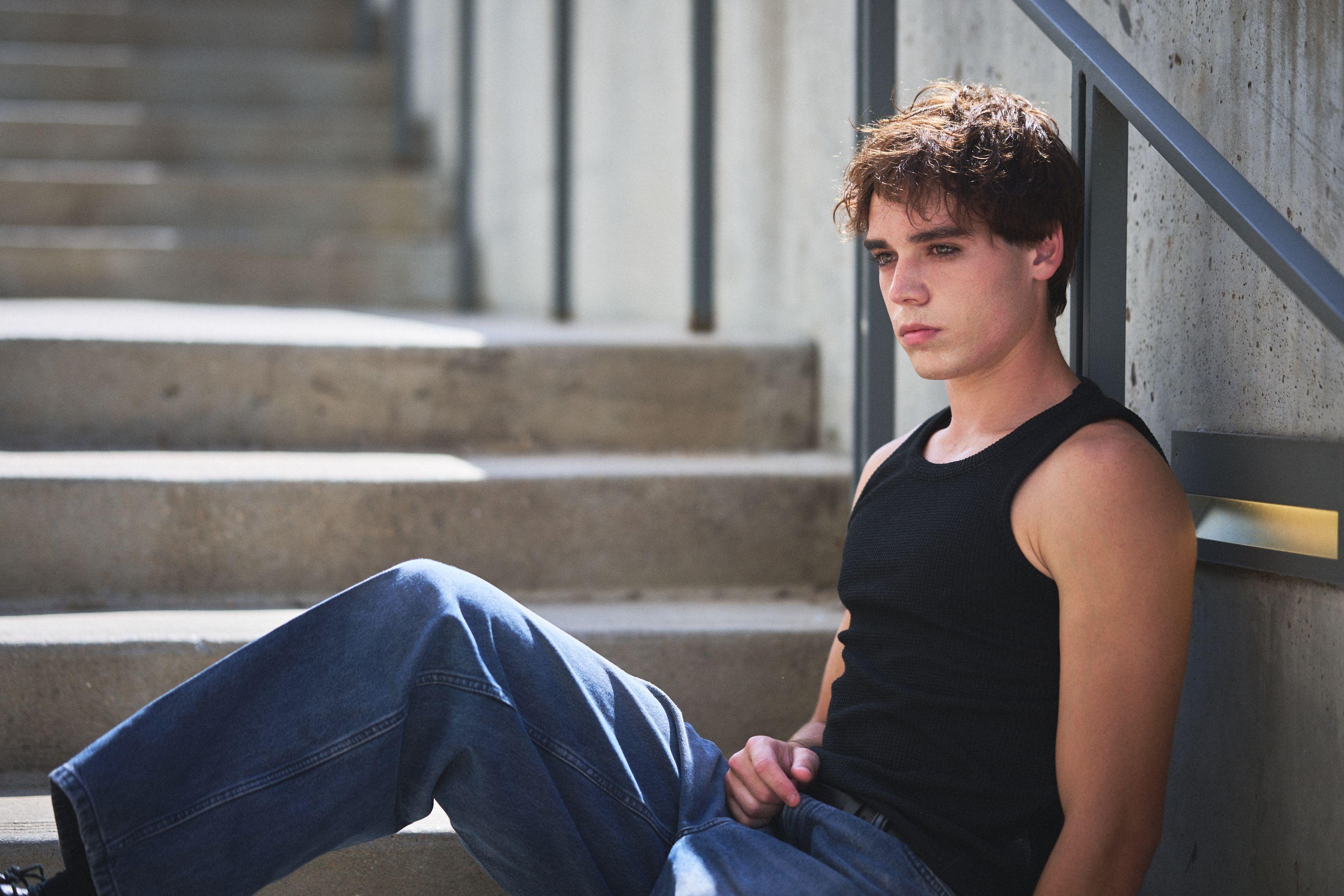 Young male model in a black tank top and jeans sitting on concrete steps — E-commerce & apparel photography, Austin Young male model in a black tank top and jeans sitting on concrete steps