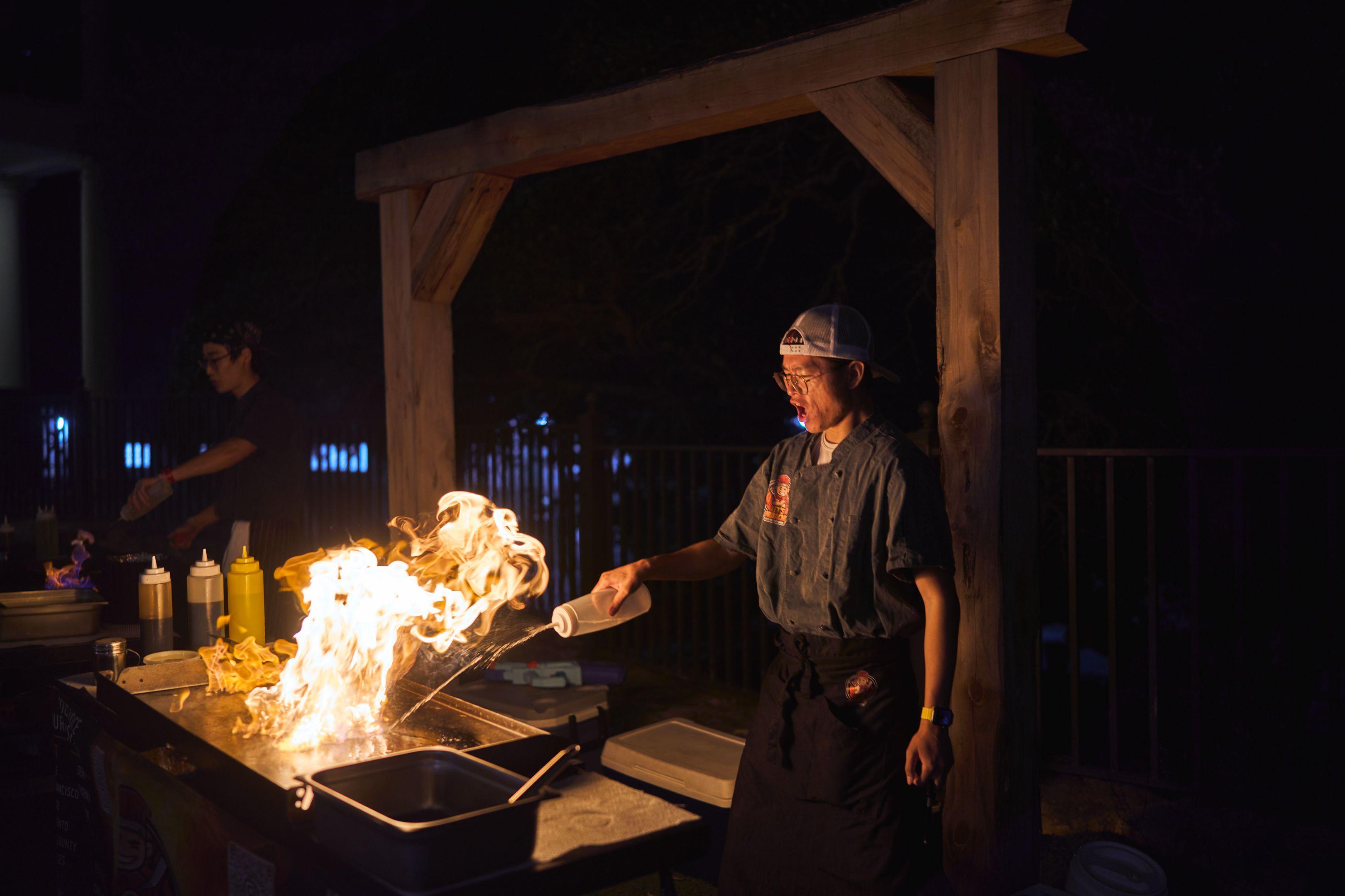 Chef working a flaming grill outdoors at night — Party & nightlife photography, Austin A chef working a flaming grill outdoors at night.