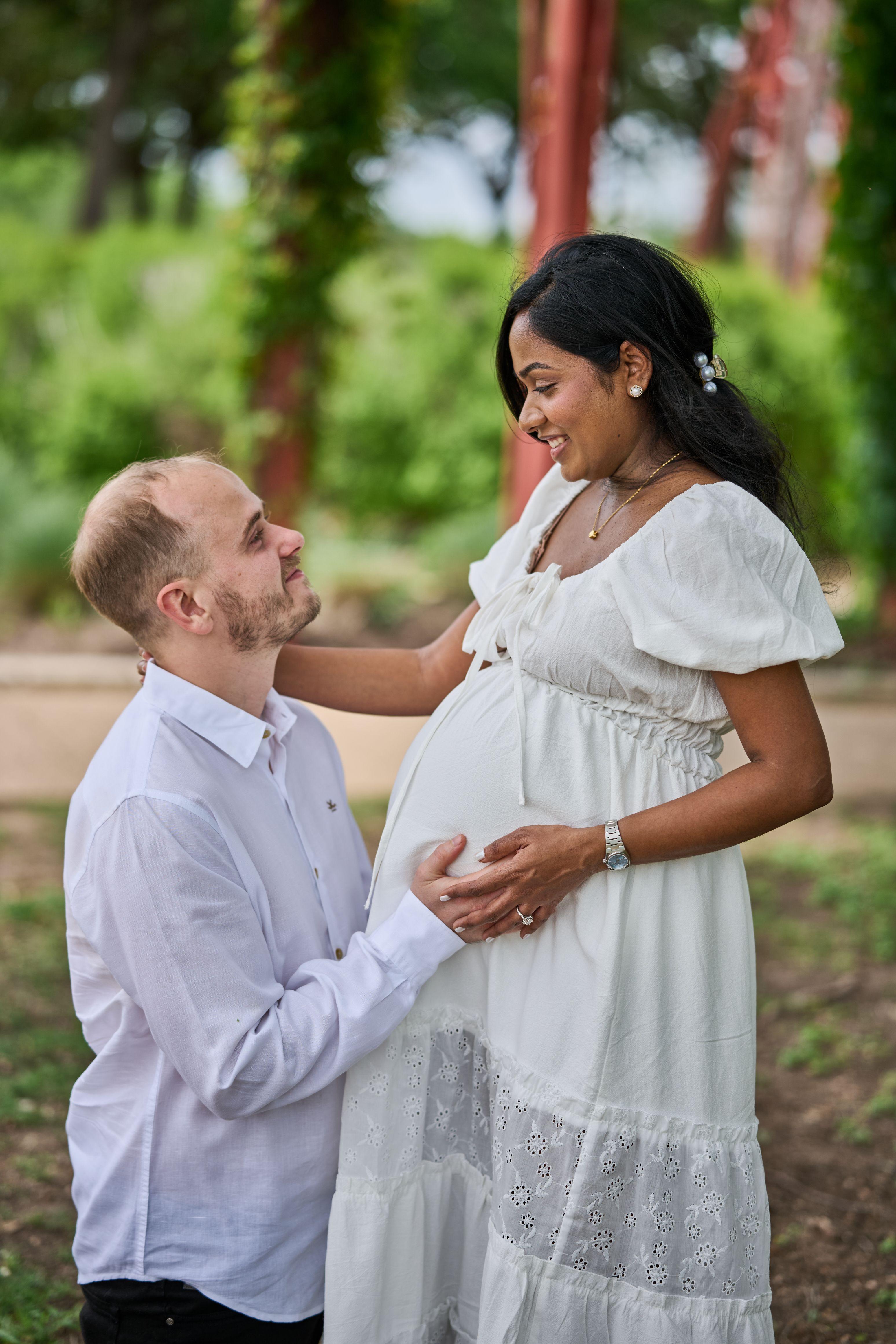 Man reaching up to an expectant mother's face beside the red pavilion columns — Mueller Lake Park & Butterfly Garden photography, Austin A man reaching up to an expectant mother's face beside the red pavilion columns at Mueller Lake Park