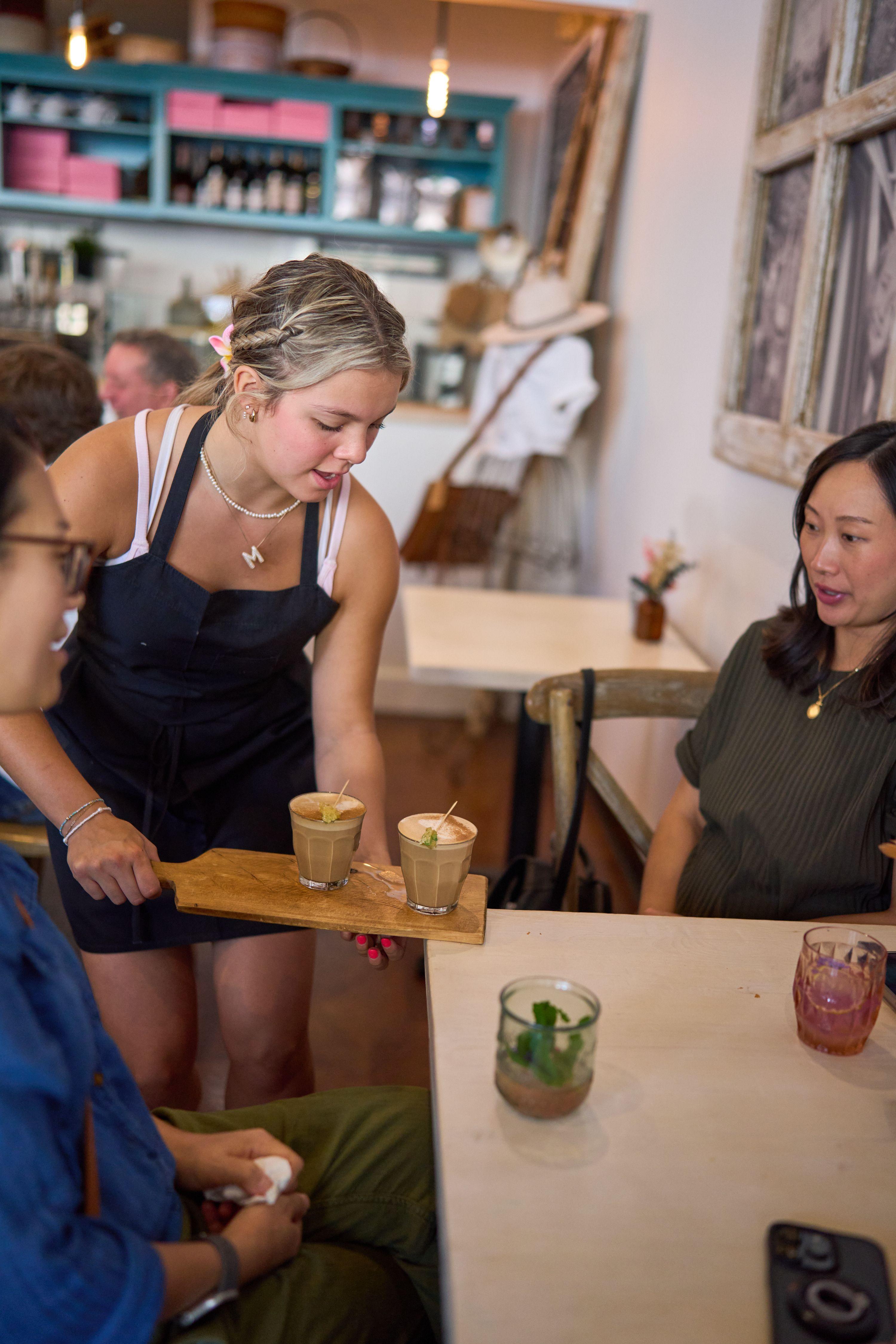 Server carrying a wooden flight of drinks past seated guests at a casual venue — Business Parties photography, Austin A server carrying a wooden flight of drinks past seated guests at a casual venue.