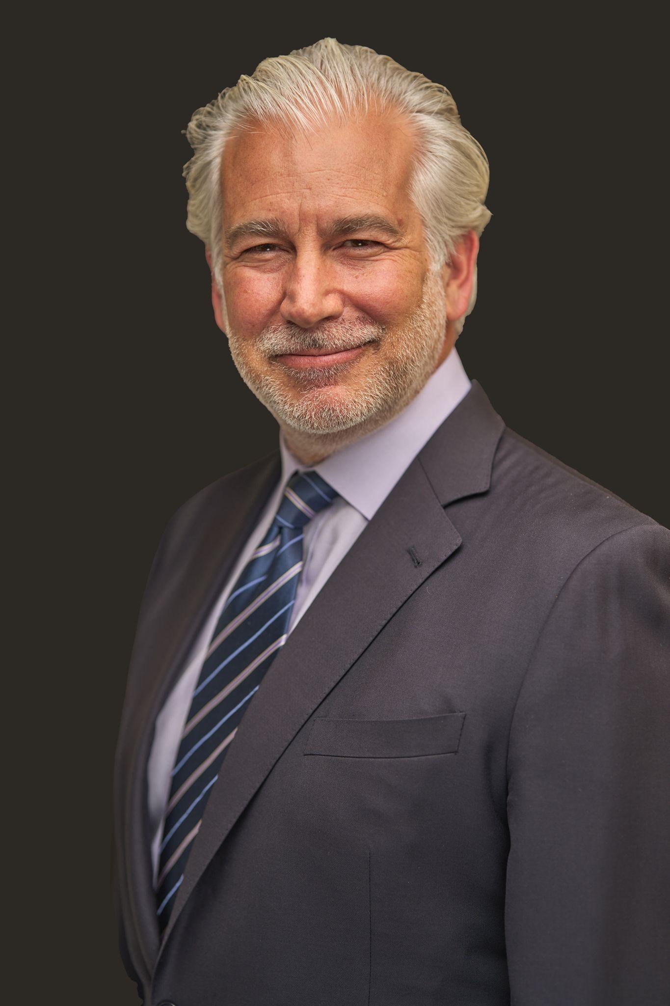 Silver-haired man in a gray suit and striped tie against a plain background — Headshot photography, Austin A silver-haired man in a gray suit and striped tie against a plain background.
