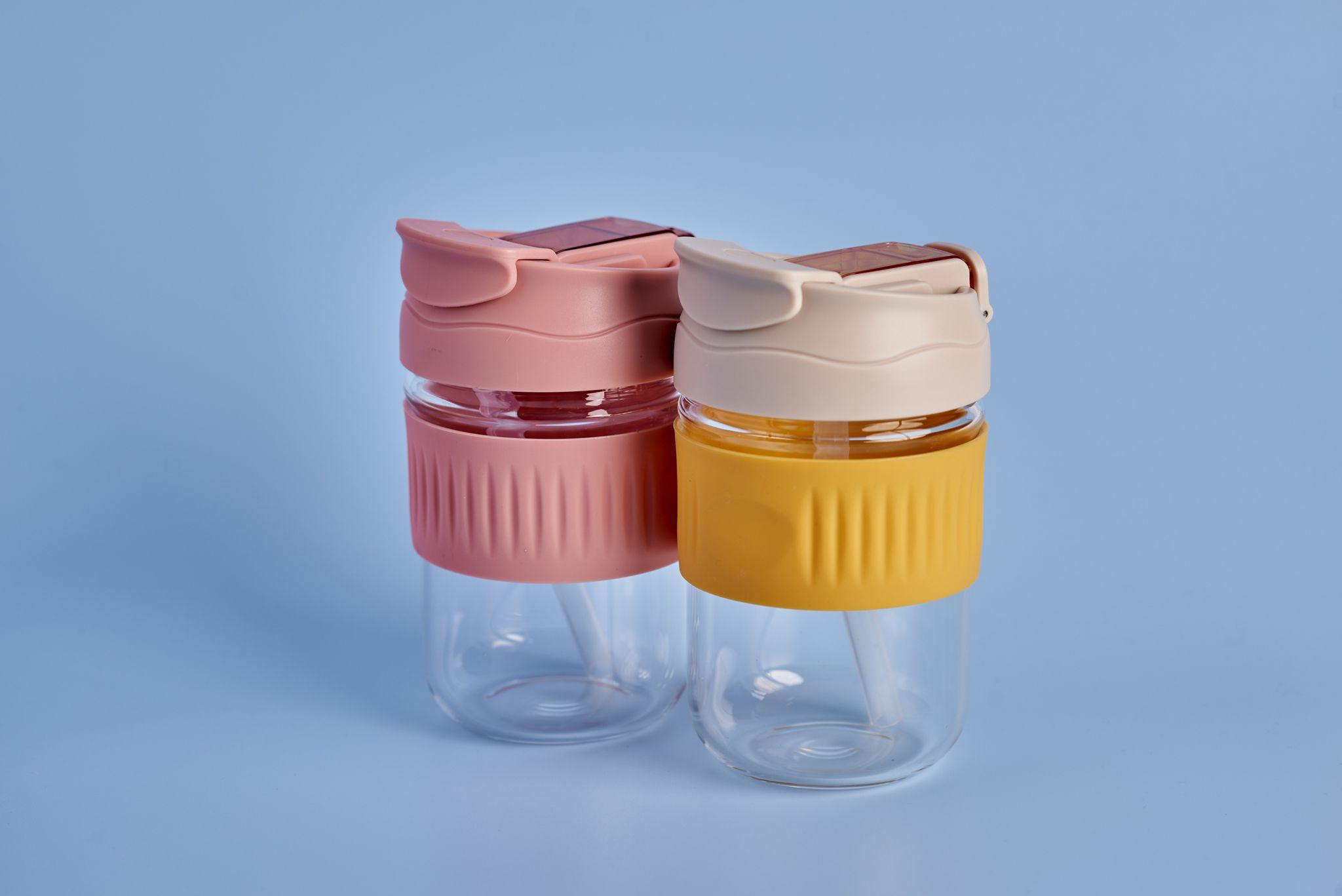 Two insulated glass tumblers with pink and cream lids on a gray background — Product photography, Austin Two insulated glass tumblers with pink and cream lids on a gray background.