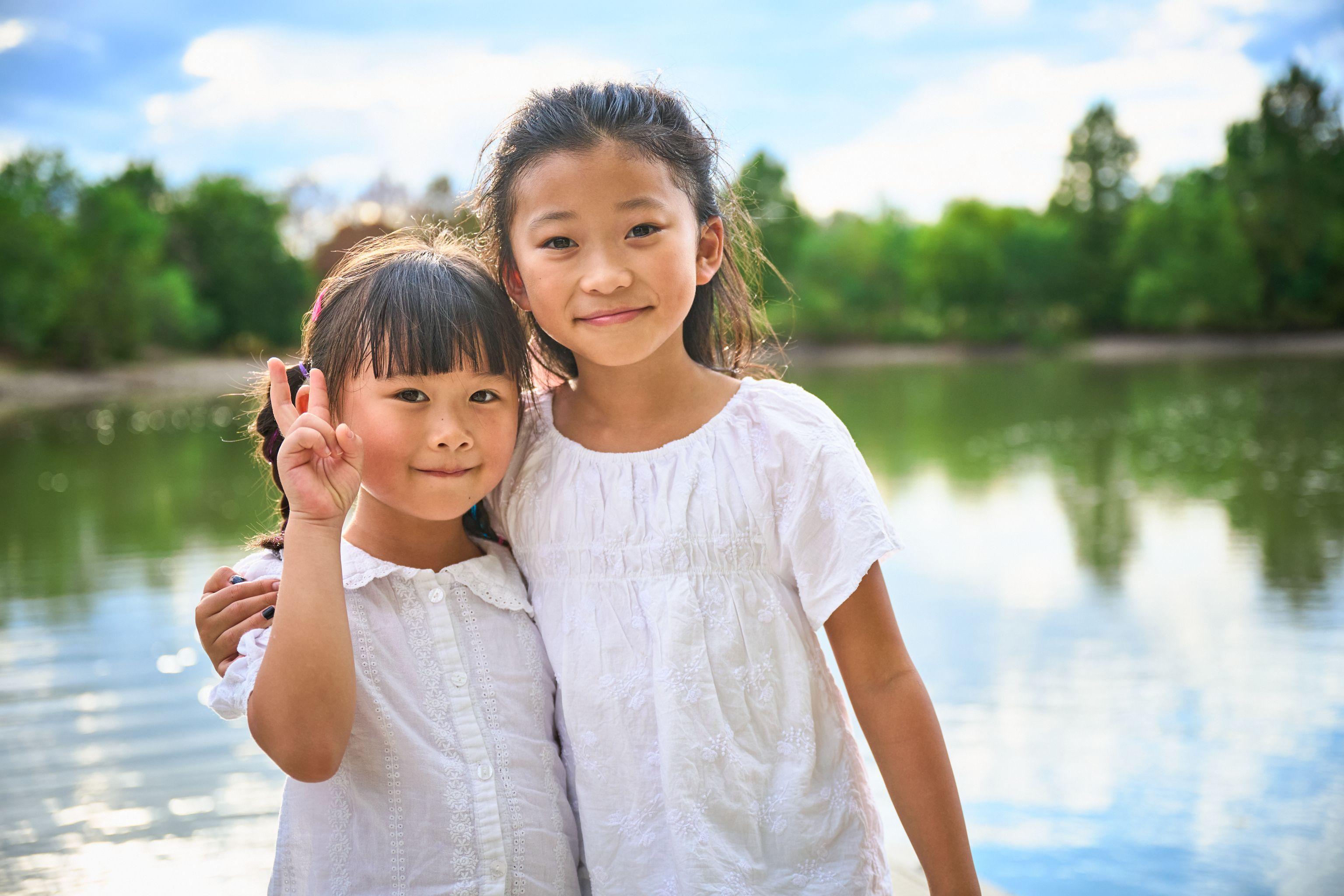 Two sisters in white blouses standing together by a lake — Kids Portraits photography, Austin Two sisters in white blouses standing together by a lake.