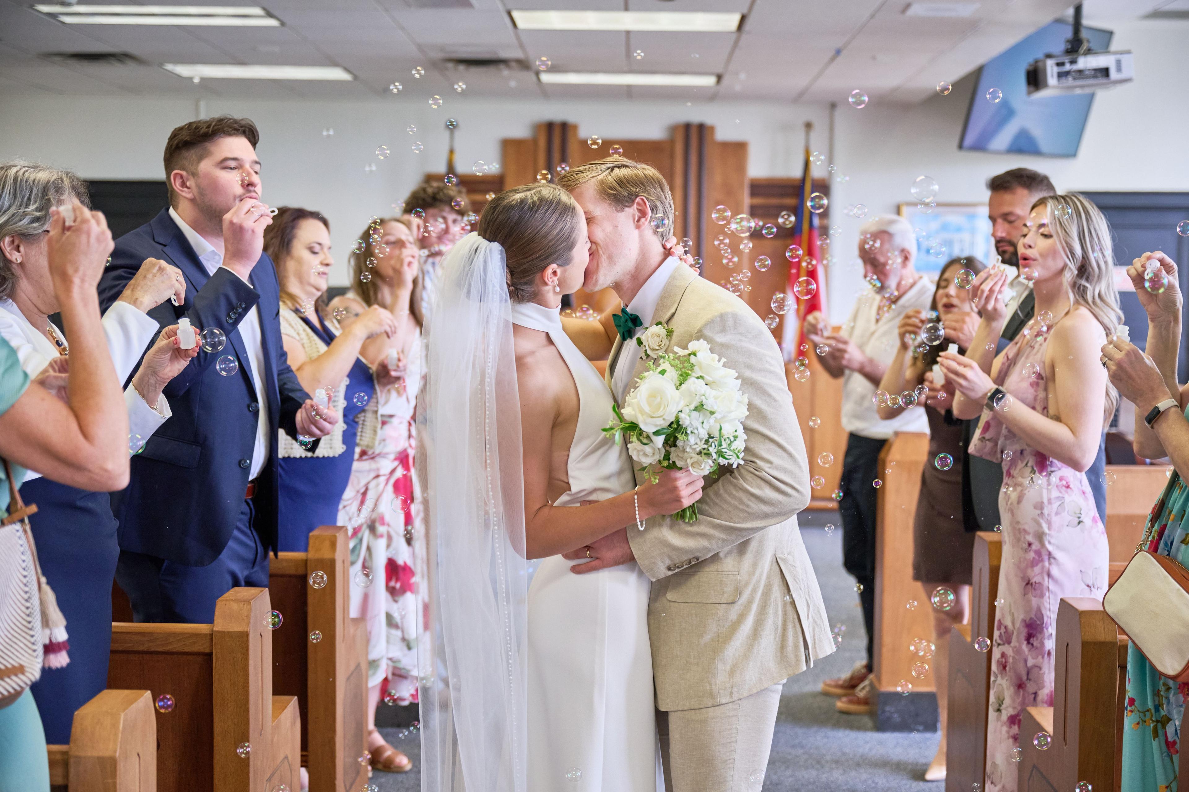 Couple kissing in the courthouse aisle as guests blow bubbles around them — Weddings photography, Austin A couple kissing in the courthouse aisle as guests blow bubbles around them.