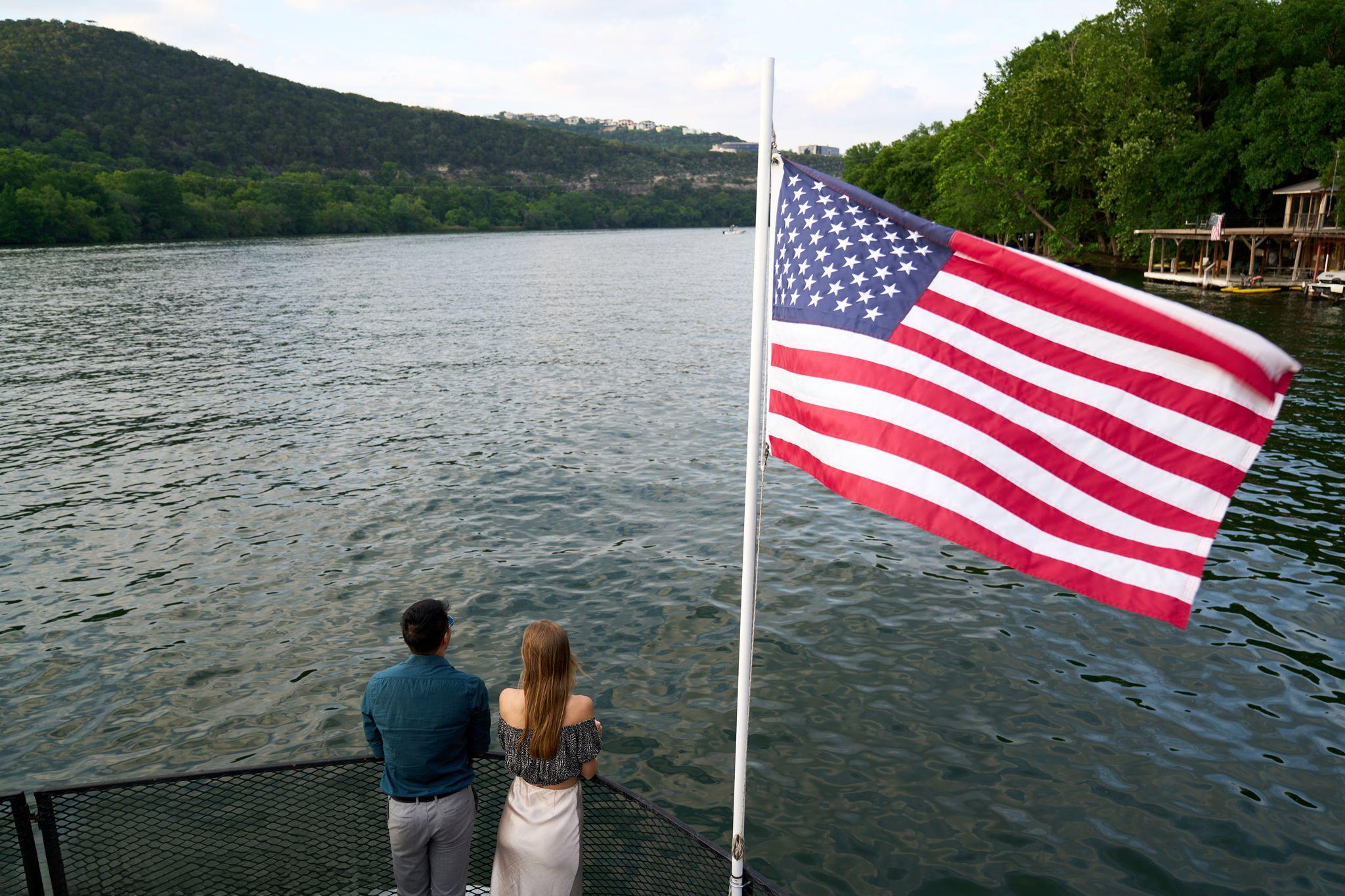 Couple standing at a railing above the lake beside an American flag — Adventure & outdoor photography, Austin A couple standing at a railing above the lake beside an American flag.