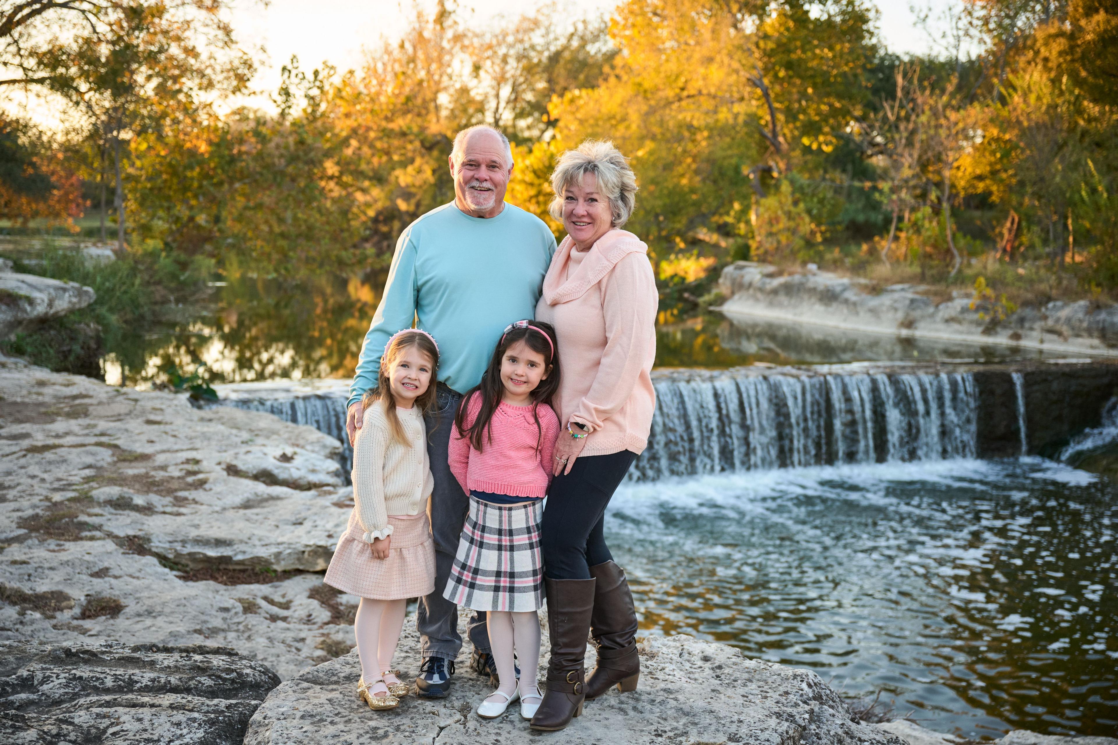 Grandparents with two granddaughters in front of a low autumn waterfall — Family Portraits photography, Austin Grandparents with two granddaughters in front of a low autumn waterfall.