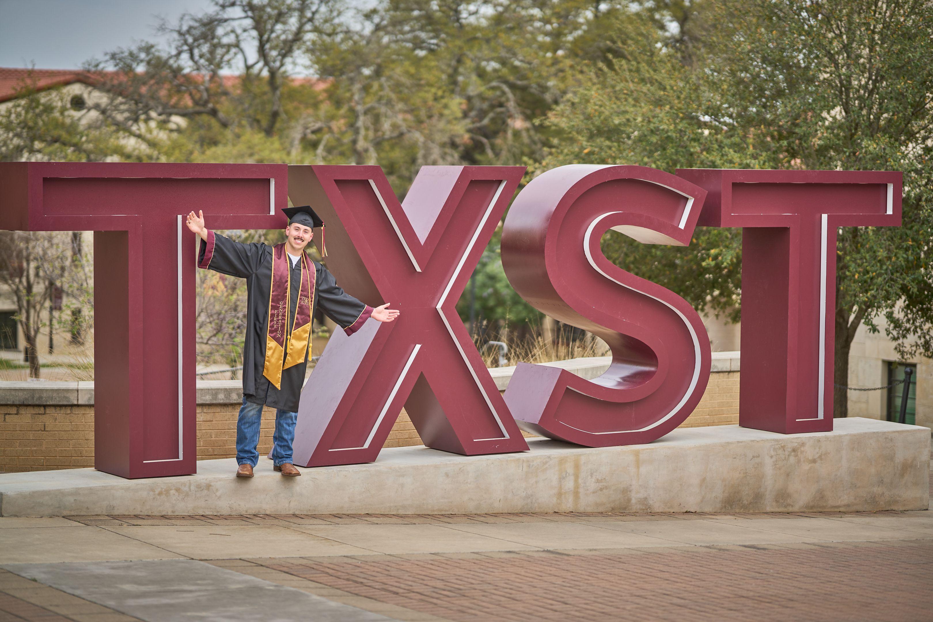 Graduate in cap and gown leaning against the giant TXS letters sculpture — Graduation & Prom photography, Austin A graduate in cap and gown leaning against the giant TXS letters sculpture.