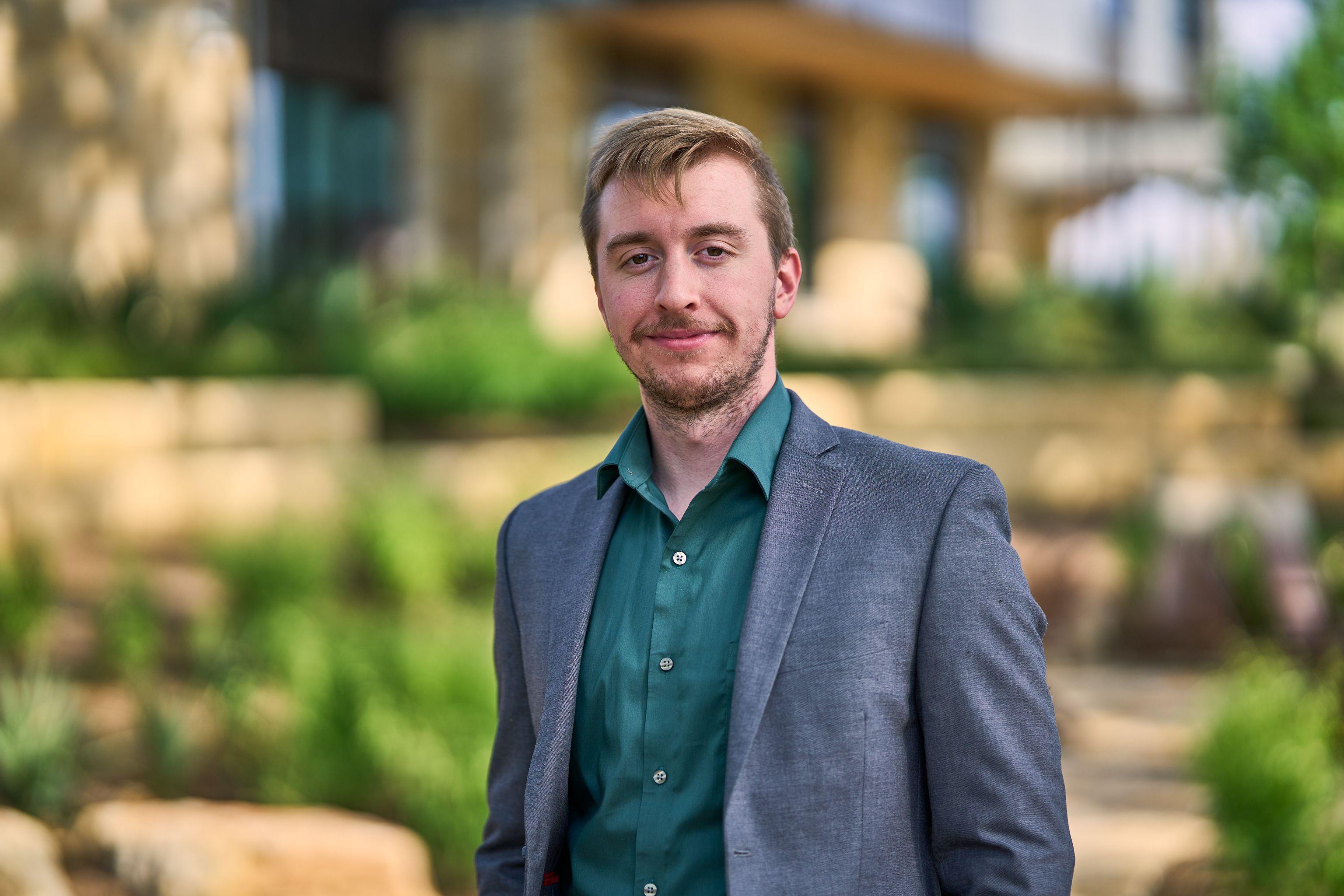 Man in a gray blazer and green shirt with the Cedar Park library building behind him — Cedar Park Public Library photography, Austin A man in a gray blazer and green shirt with the Cedar Park library building behind him