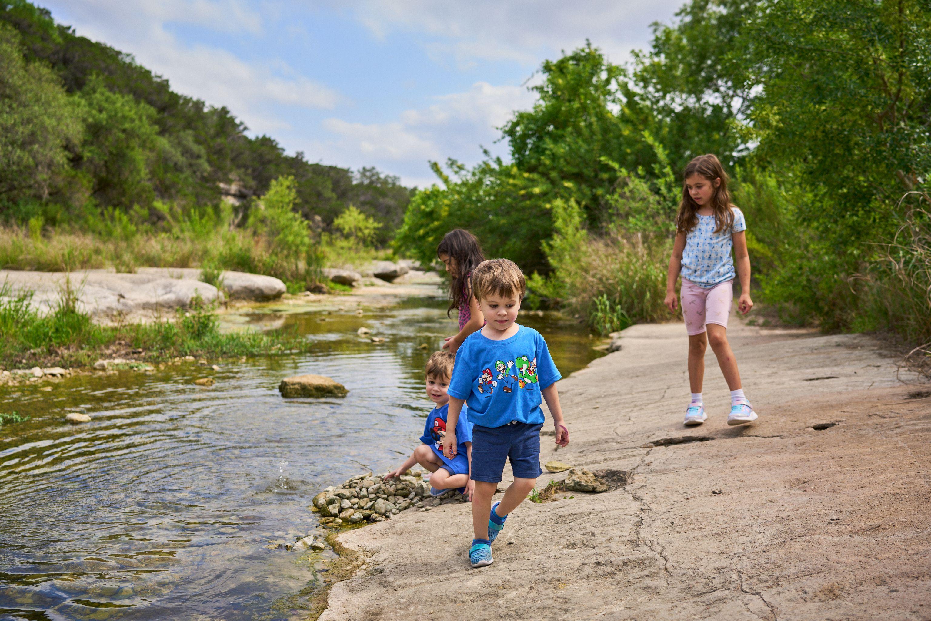 Boy walking along a limestone creek bed while his family sits further back — Bull Creek District Park photography, Austin A boy walking along a limestone creek bed while his family sits further back.