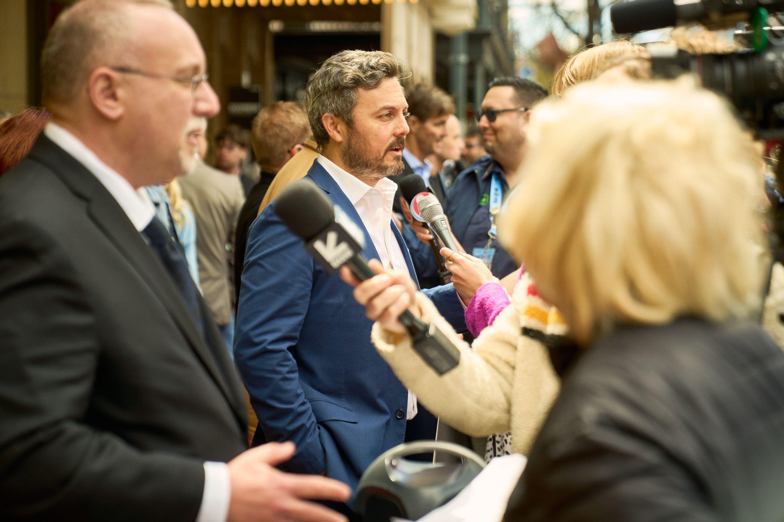Interviewee surrounded by outstretched microphones and press at an outdoor media scrum — Production behind-the-scenes, Austin Interviewee surrounded by outstretched microphones and press at an outdoor media scrum