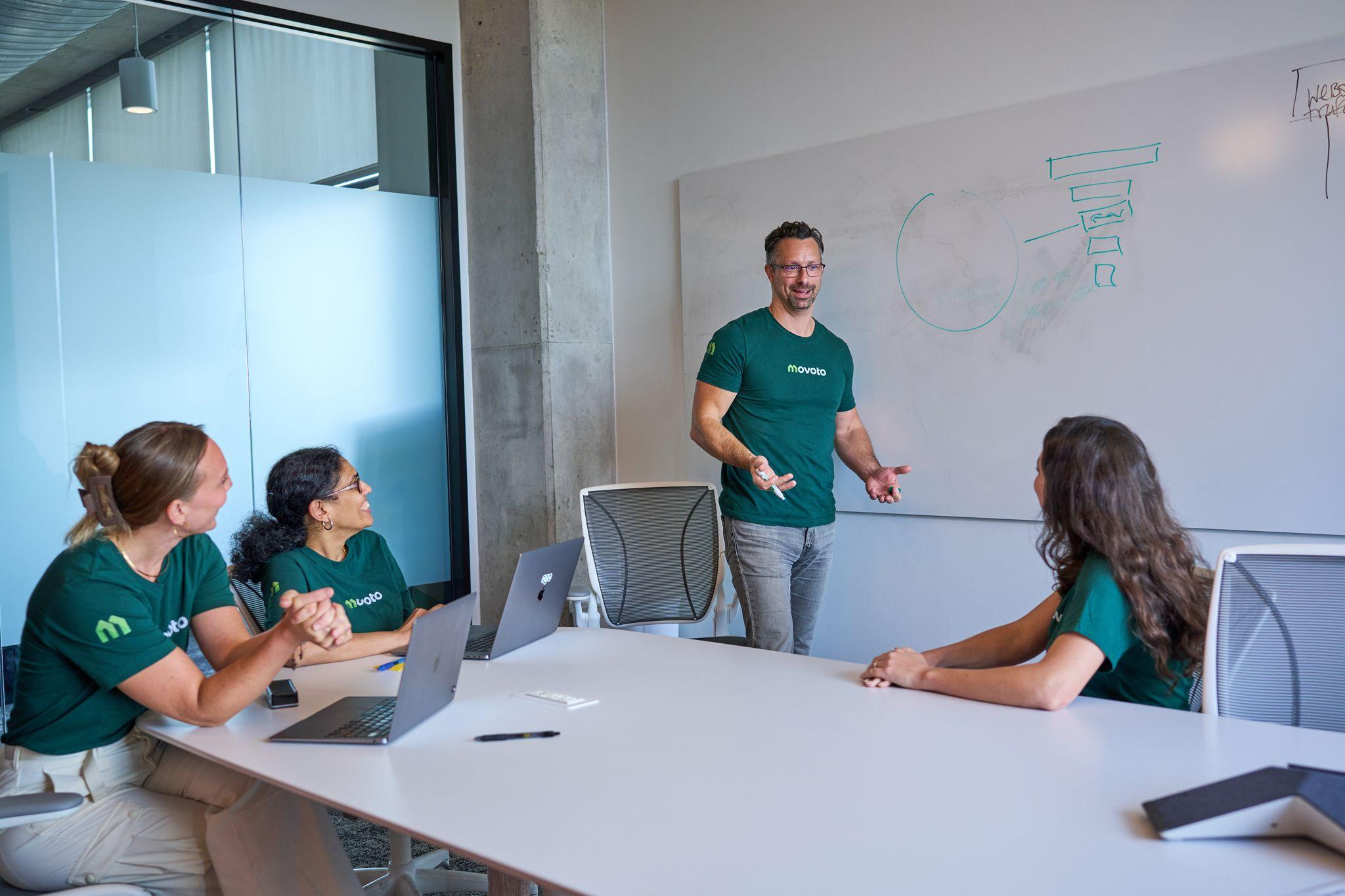 A man presenting at a whiteboard in a concrete-walled meeting room